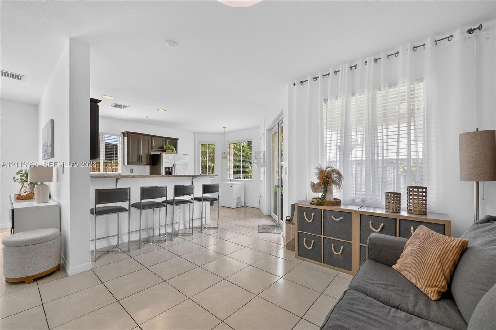 Open-concept interior featuring light-toned tile flooring, recessed lighting, a kitchen breakfast bar, and glass-paned sliding doors