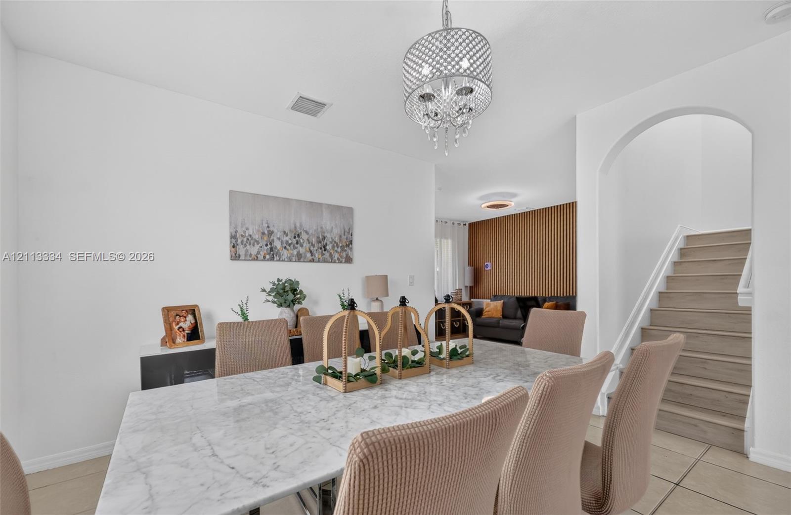 Dining area featuring a circular crystal chandelier, arched entryway, staircase with wood-finish treads, and vertical wood slat accent wall