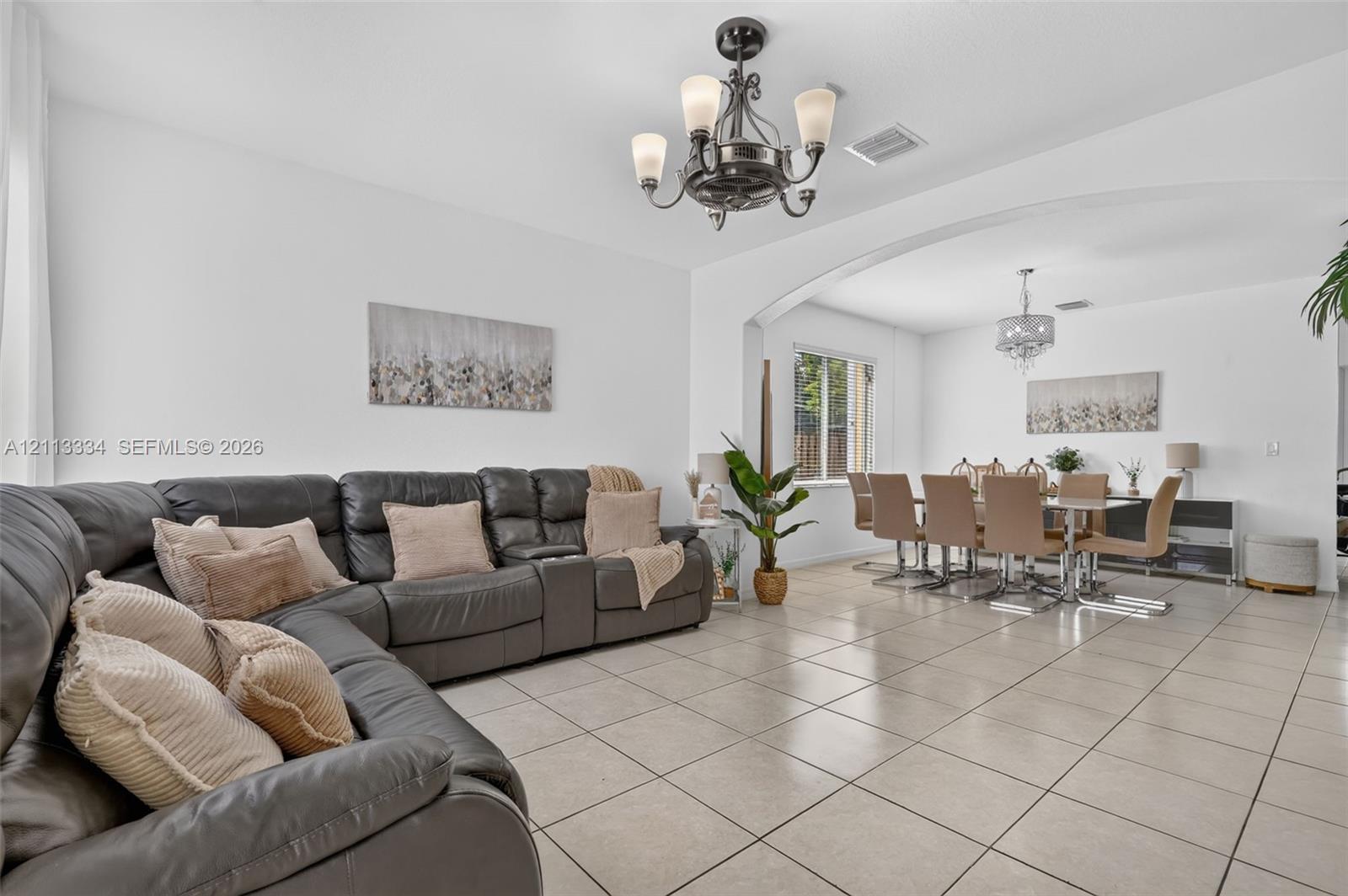Neutral tile flooring, arched wall detailing, wrought-iron style multi-light chandelier, and decorative ceiling light fixtures