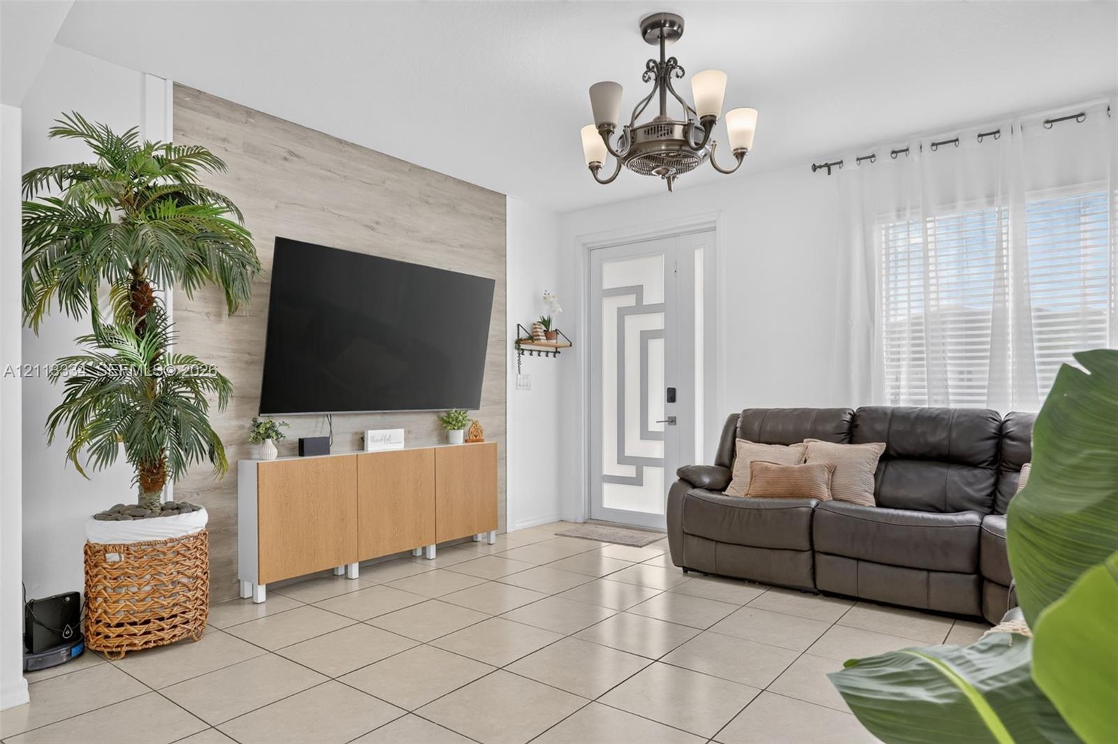 Living area featuring large-format tile flooring, a prominent wood-finish accent wall, a decorative five-light chandelier, and an exterior door with geometric glass paneling