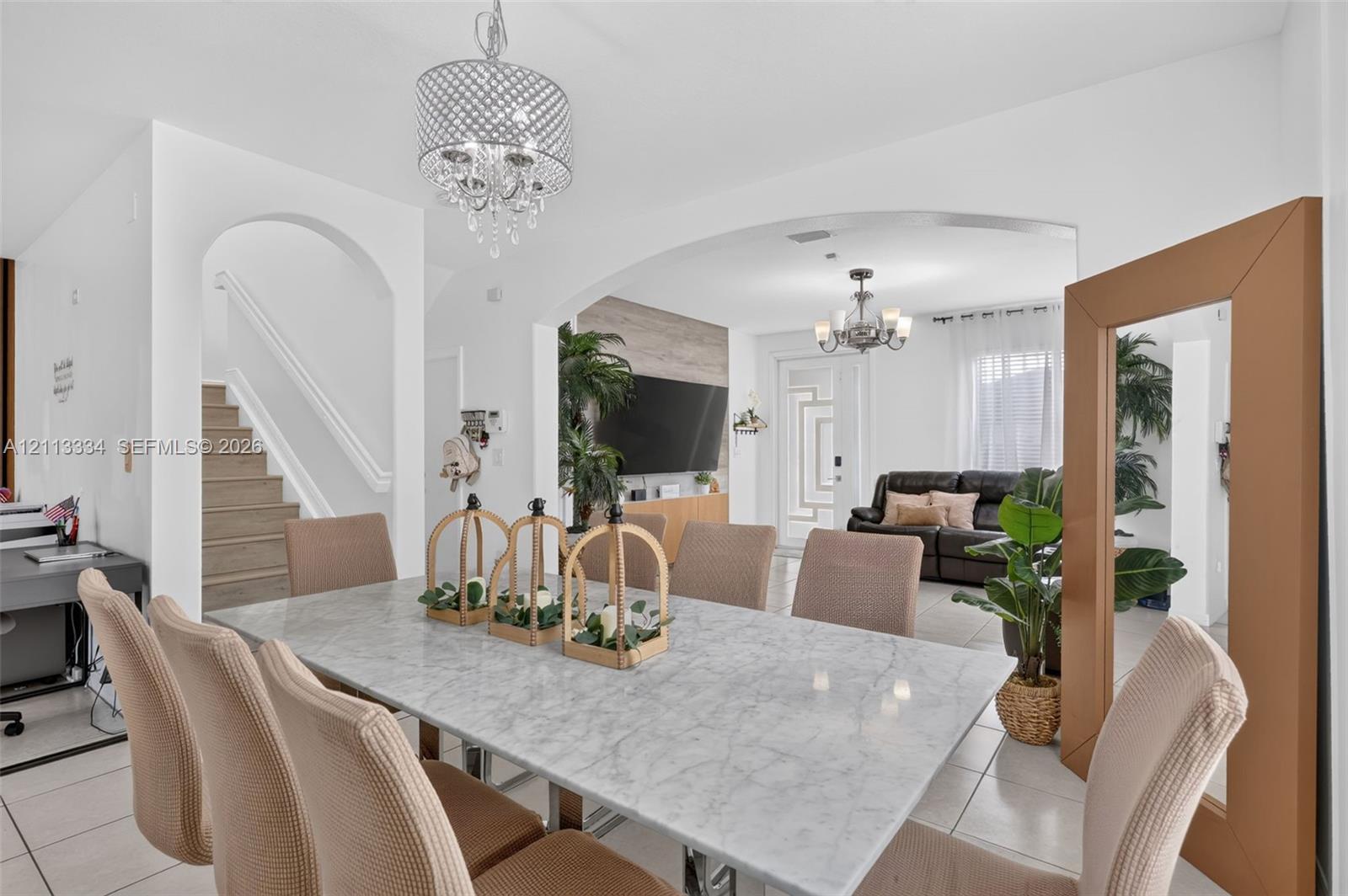 Open-concept interior featuring arched architectural detailing, tile flooring, and decorative multi-tiered pendant lighting