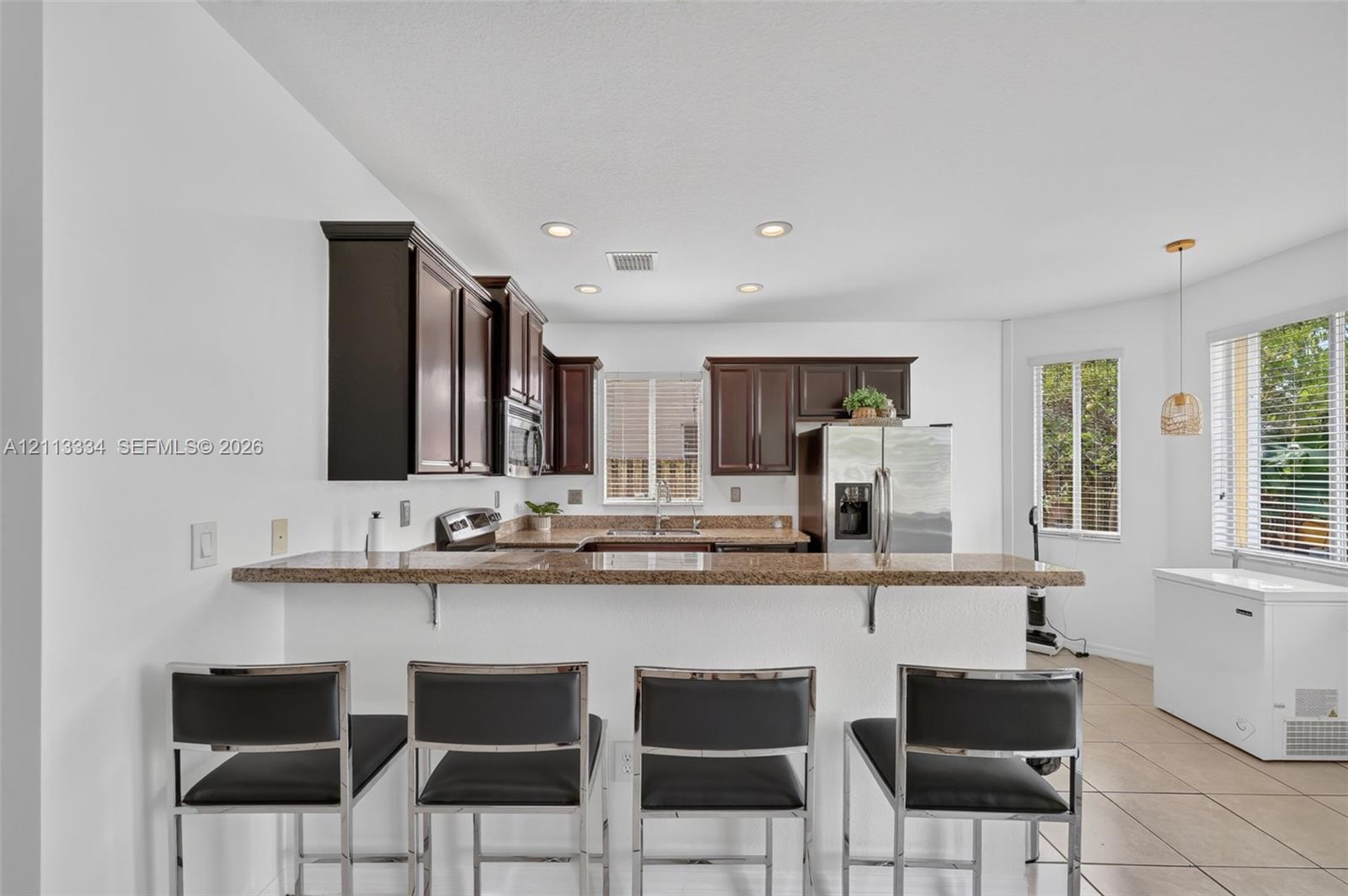 Kitchen featuring dark-toned cabinetry, stone-finish countertops, a breakfast bar, recessed lighting, and tile flooring