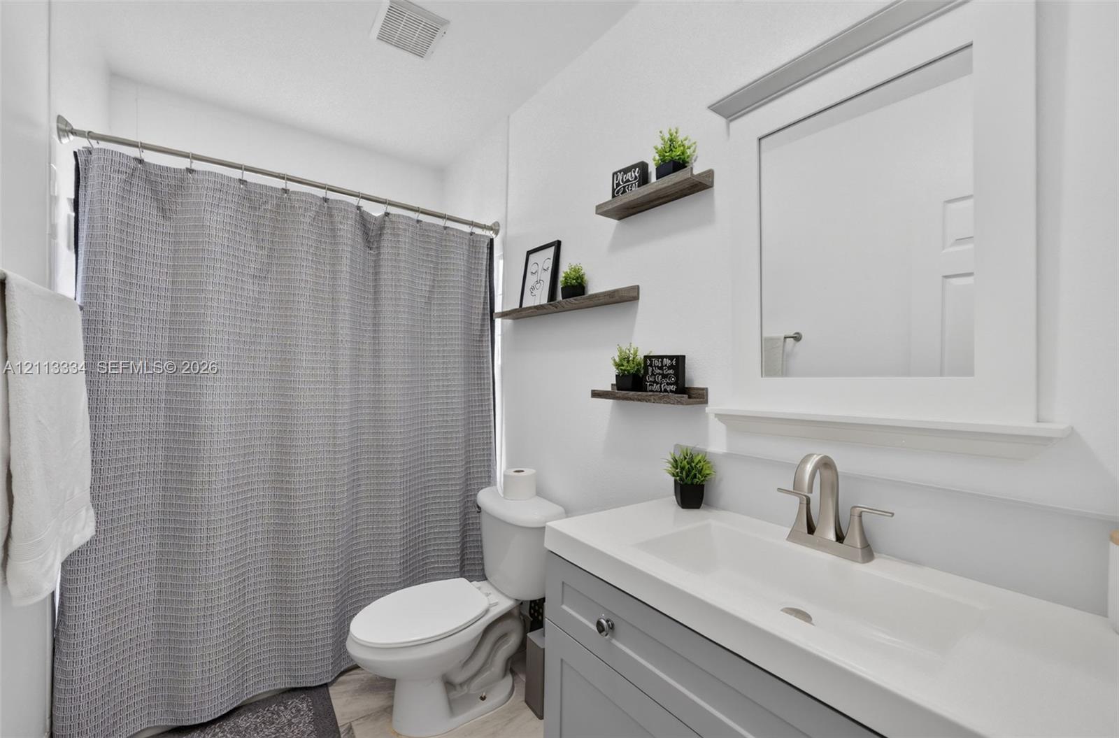 Bathroom featuring a vanity with a white countertop and integrated sink, brushed-nickel faucet, framed mirror, and three wall-mounted wood-finish floating shelves