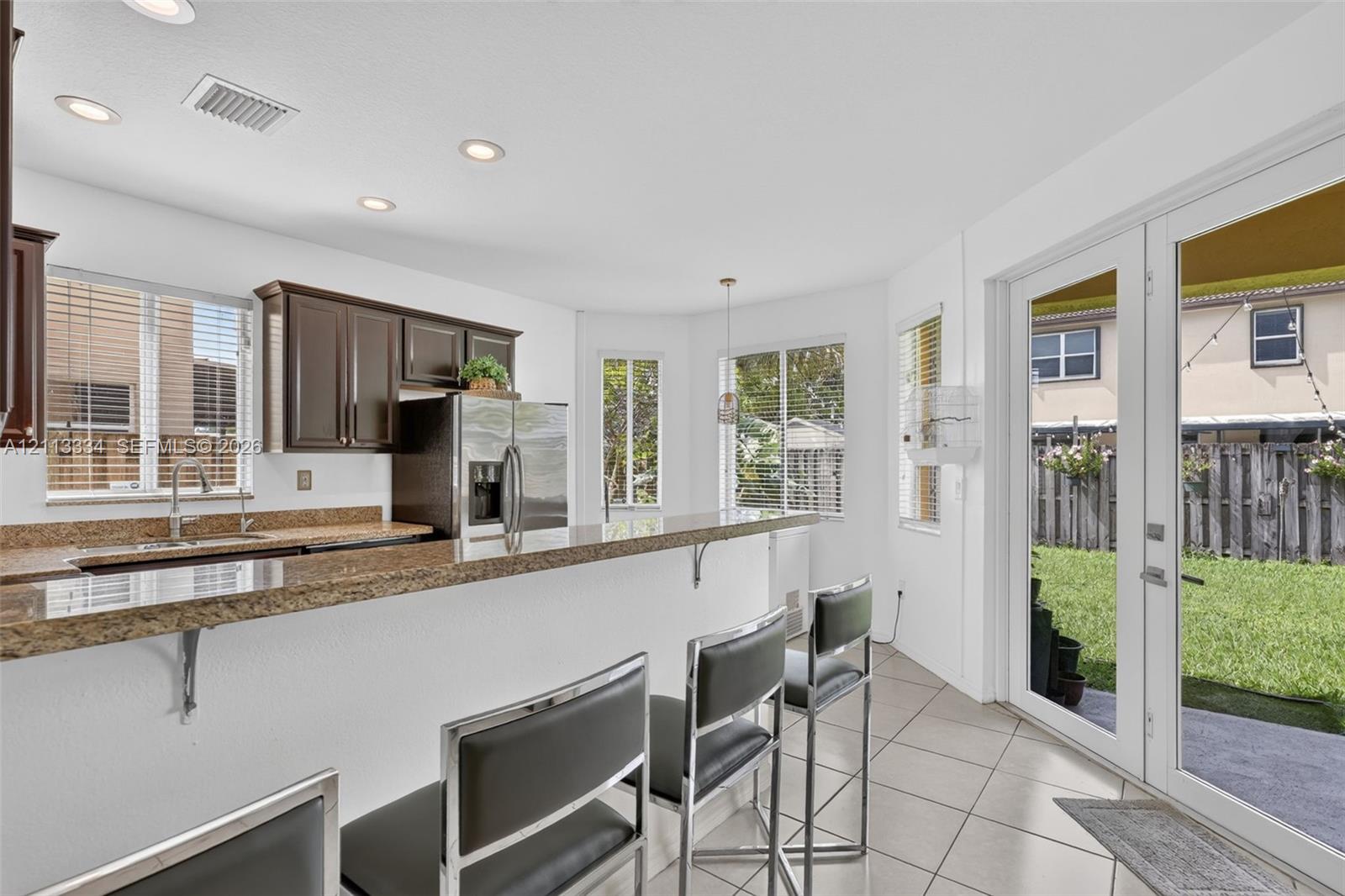 Kitchen featuring stone countertops, dark wood cabinetry, recessed lighting, tile flooring, and glass-paneled double doors providing rear exterior access