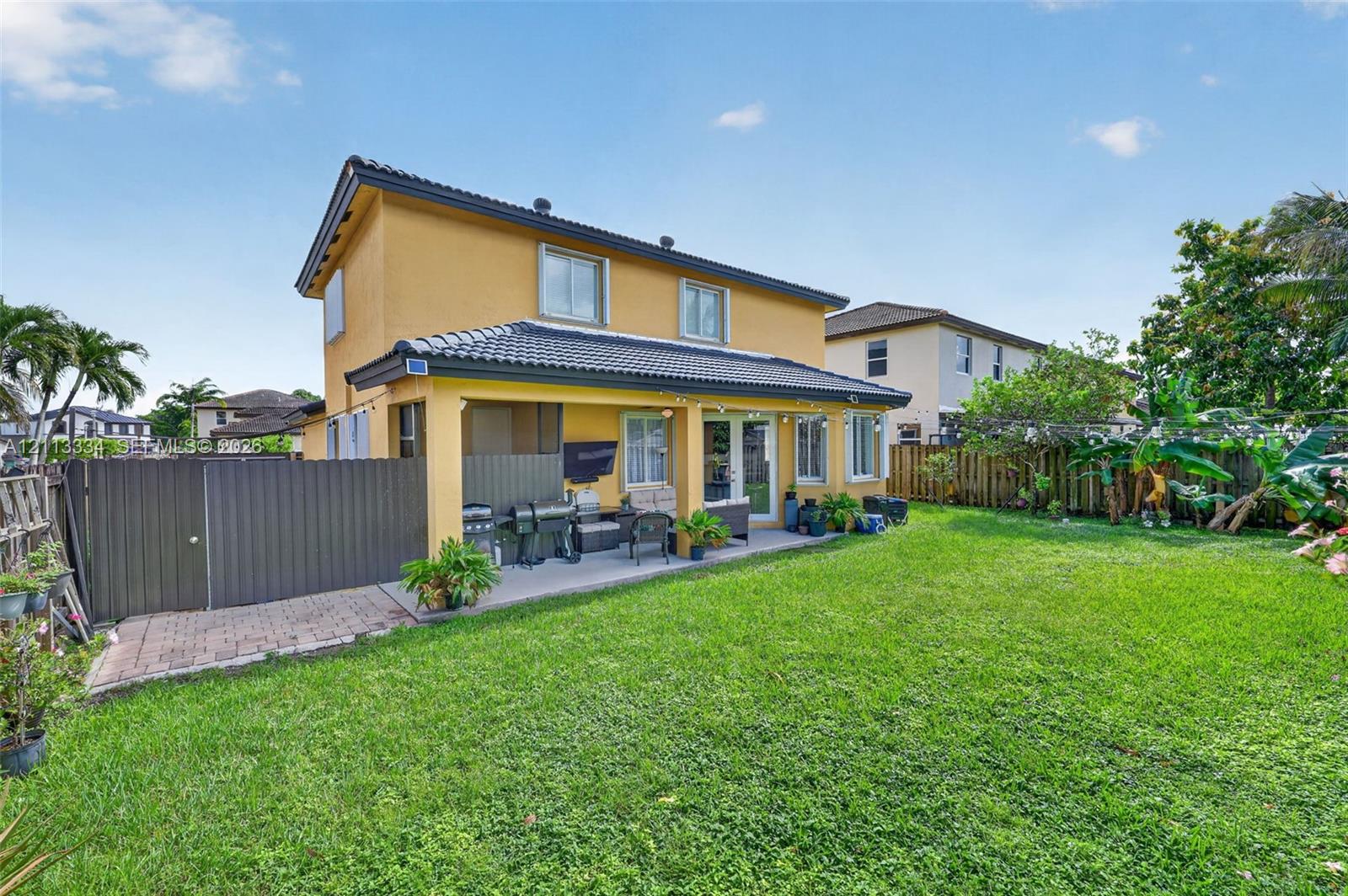 Two-story exterior with a tiled roof, a covered concrete patio, and a fenced backyard