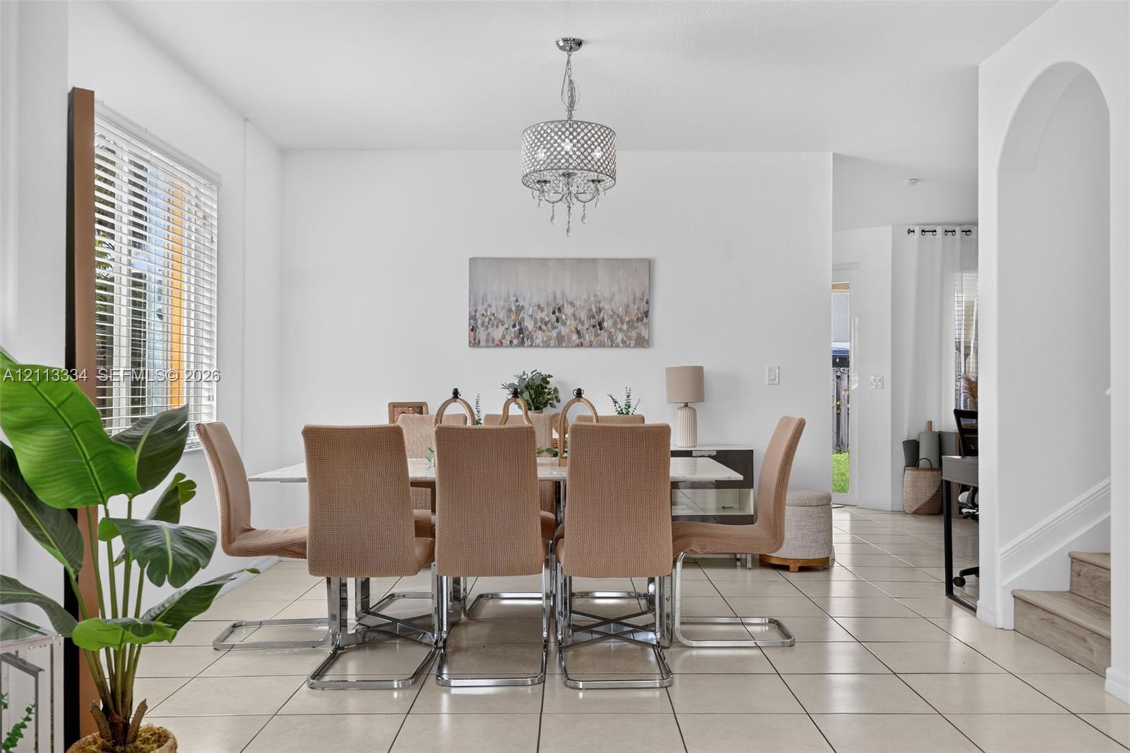 Dining area featuring neutral tile flooring, a multi-light drum chandelier, an arched entryway, and white walls