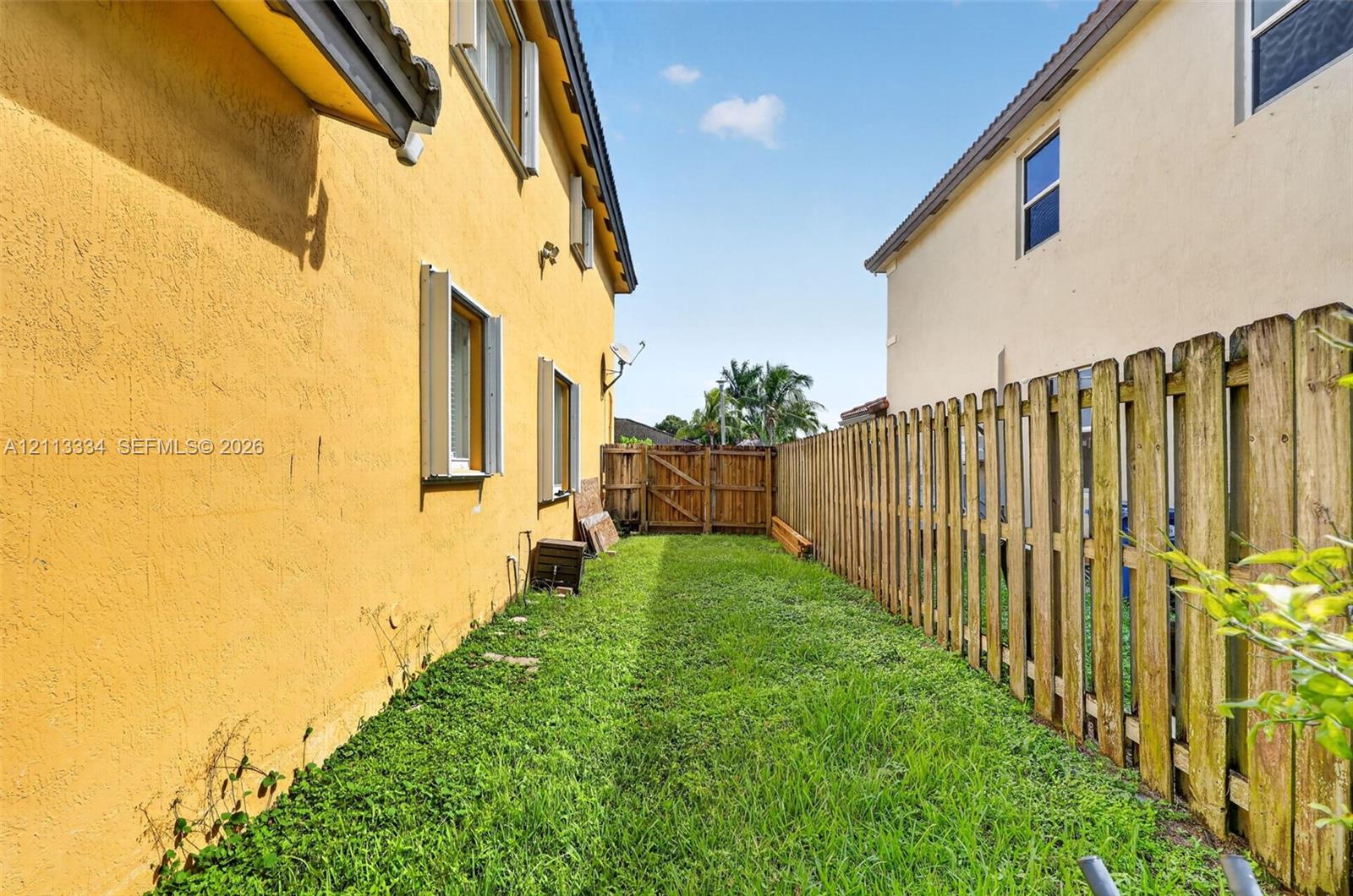 Exterior side yard featuring stucco siding, grass lawn, and a wooden privacy fence with a gated entry