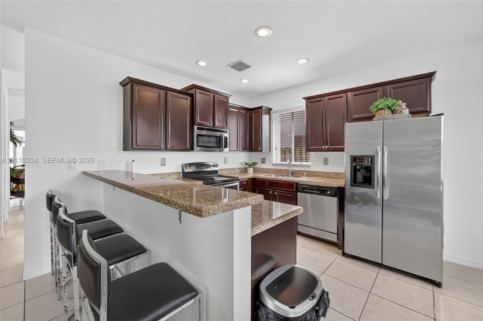Kitchen featuring dark wood cabinetry, stone-surface countertops, breakfast bar, recessed lighting, and stainless steel appliances