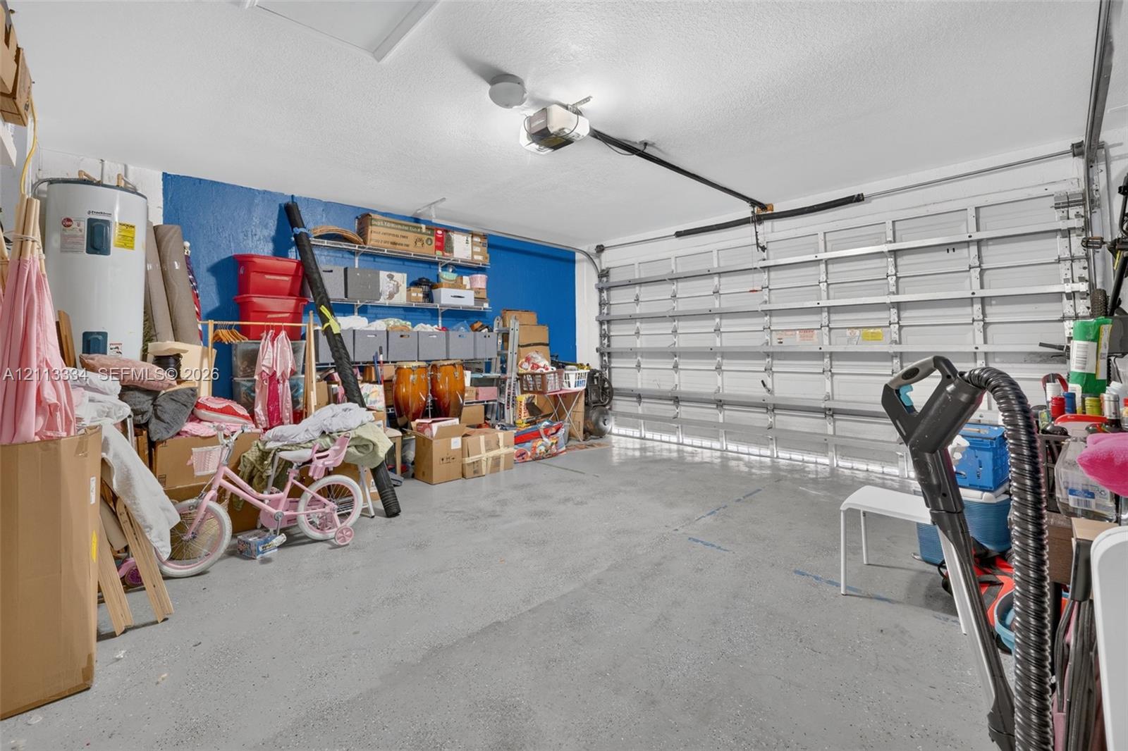 Two-car garage featuring a sectional overhead door, automated door opener, wall-mounted storage shelving, and a water heater