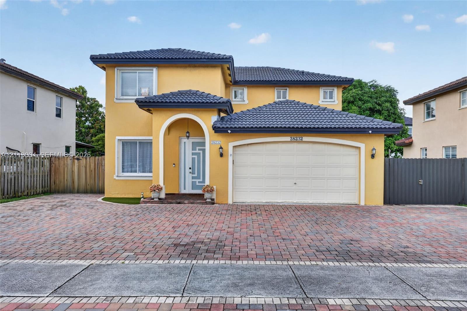 Two-story exterior featuring a tile roof, an arched entry, a geometric glass-panel front door, and a multi-car brick paver driveway Two-story exterior featuring a tile roof, an arched entry, a geometric glass-panel front door, and a multi-car brick paver driveway