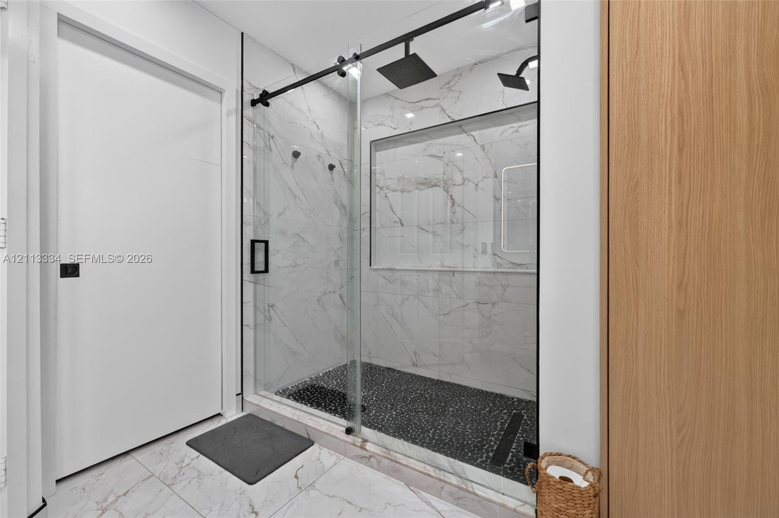 Walk-in shower featuring large-format wall tiling, a sliding glass door, matte black hardware, a rainfall showerhead, and a recessed wall niche