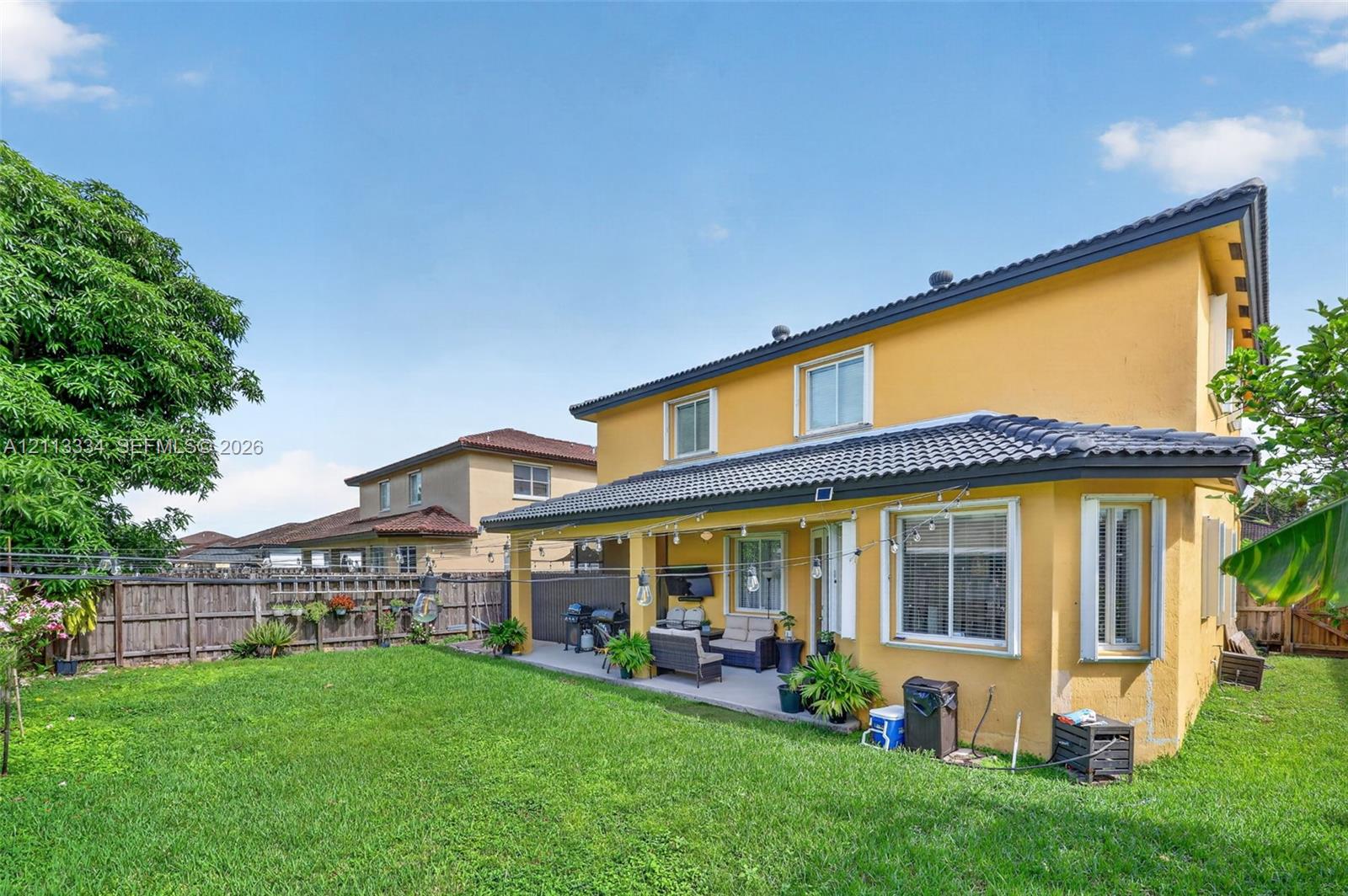 Stucco exterior residence featuring a covered concrete patio, tile roof, and a fenced backyard with lawn
