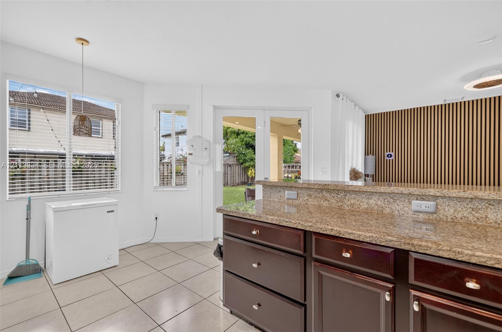 Kitchen featuring dark-toned cabinetry, stone-finish countertops, tile flooring, decorative vertical wood-slat wall paneling, and glass-paneled doors
