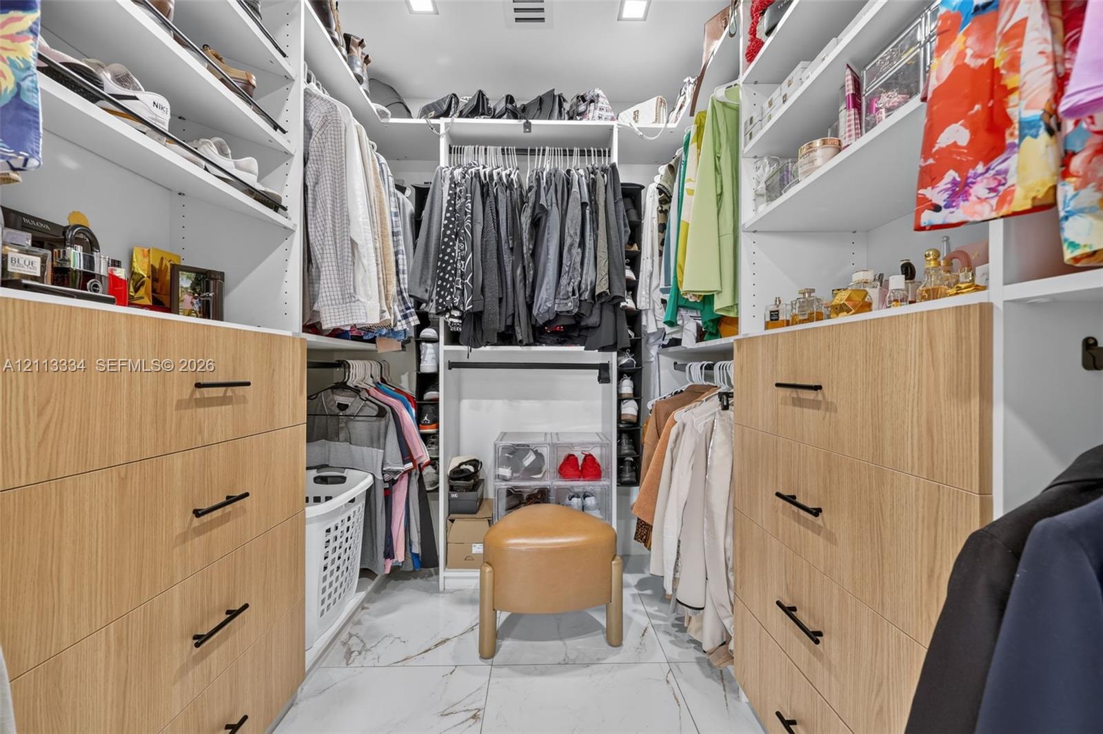 Custom walk-in closet featuring white built-in shelving, wood-finish cabinetry, matte black hardware, and stone-finish flooring