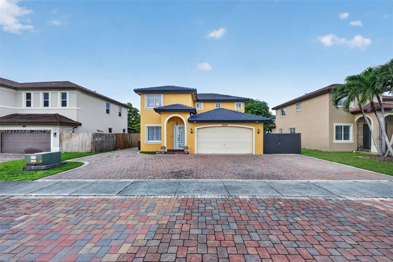 Two-story residence featuring a tile roof, stucco exterior, arched entryway, and a multi-car garage with a paver driveway