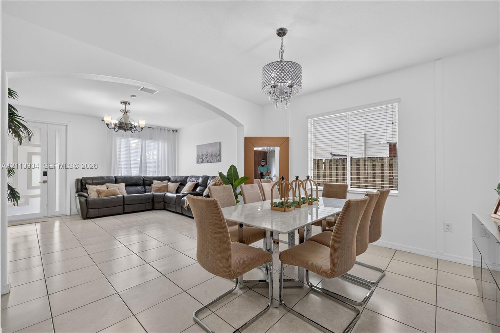 Open-concept interior featuring large-format ceramic tile flooring, arched architectural detailing, and two decorative crystal-style chandeliers
