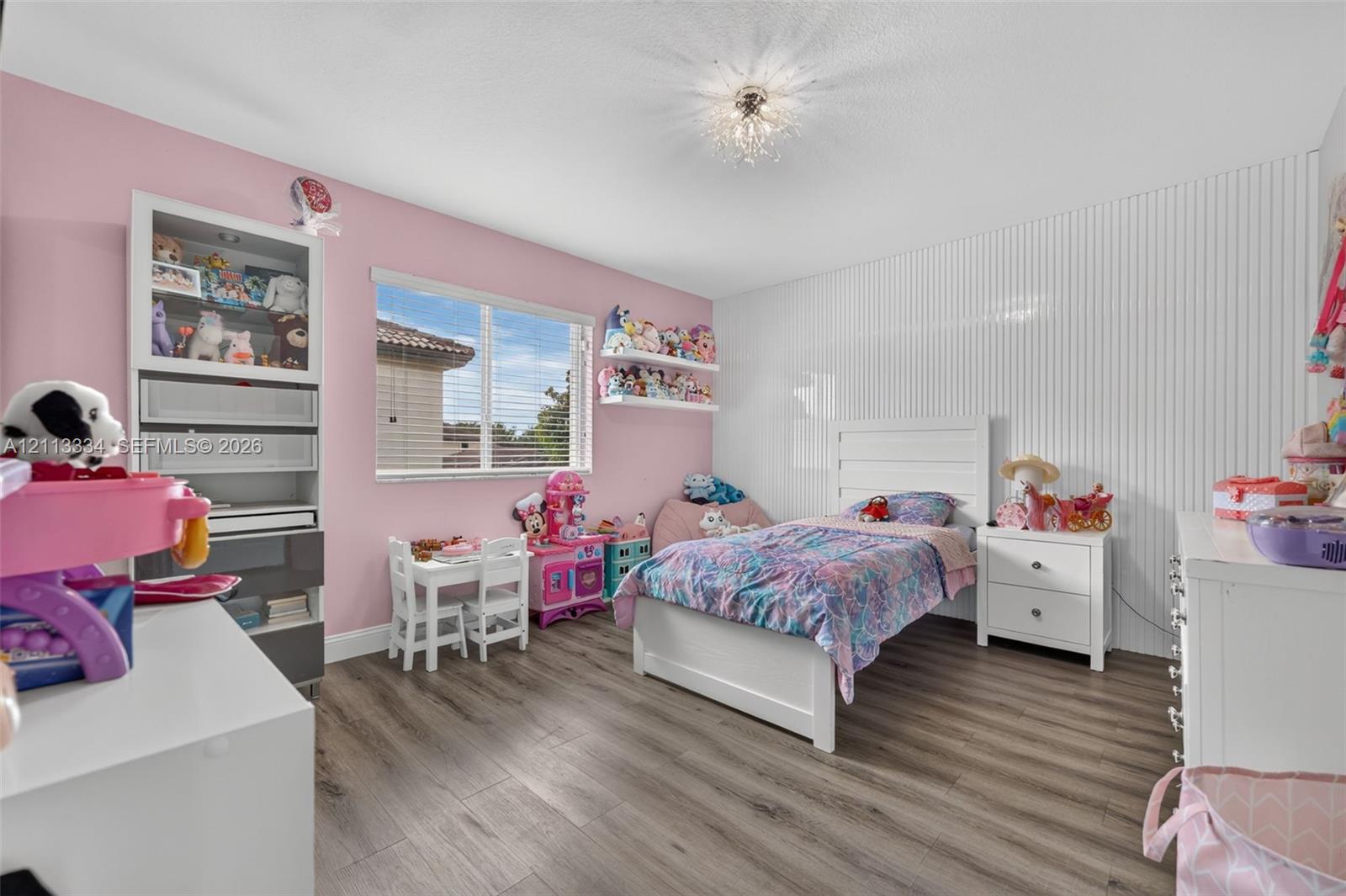 Wood-finish flooring, vertical slat wall paneling, built-in recessed shelving unit, and a ceiling-mounted crystal-style light fixture