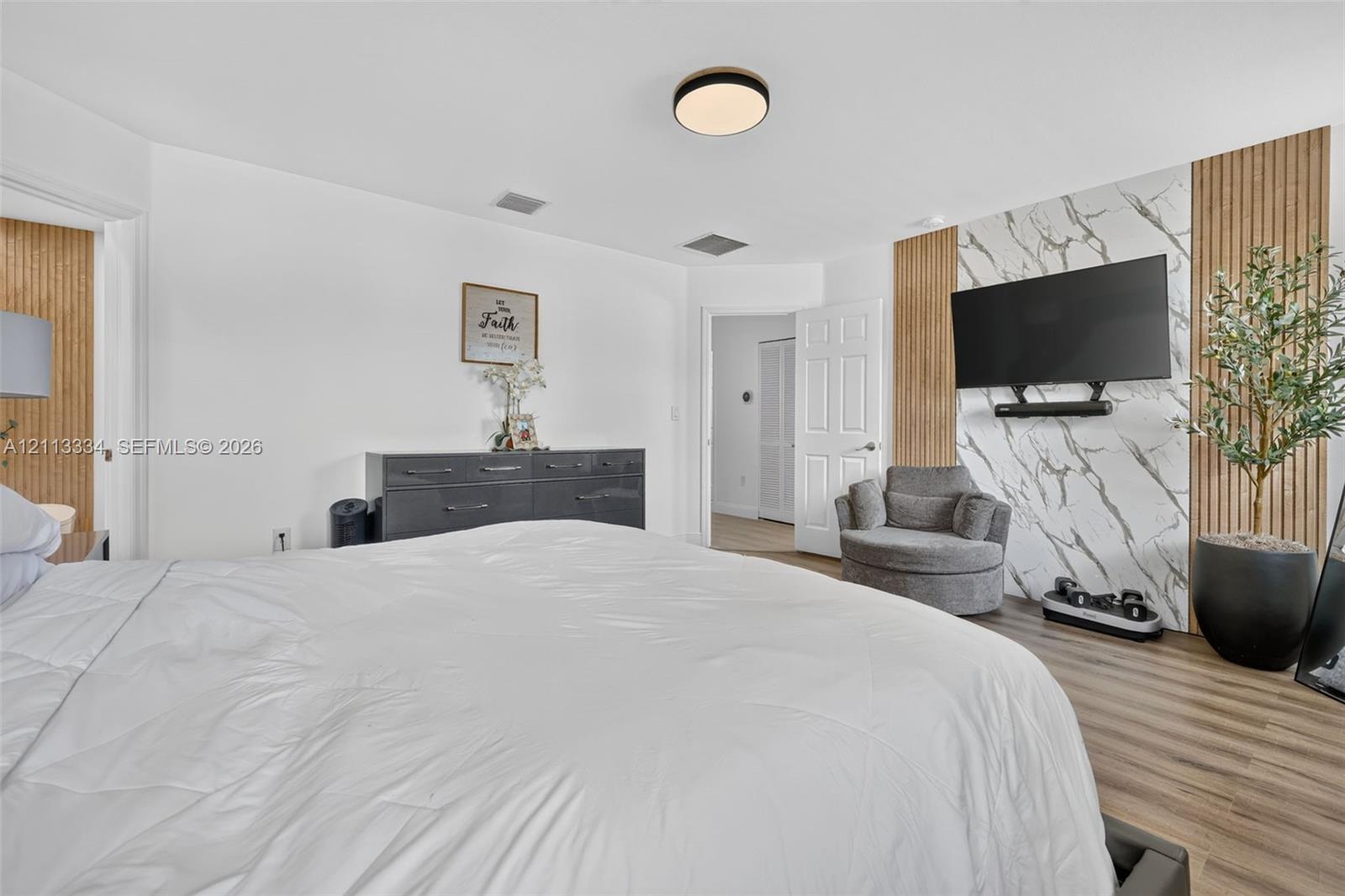 Wood-finish flooring, accent wall featuring vertical wood slat detailing, stone-finish paneling, and a flush-mount circular ceiling light fixture