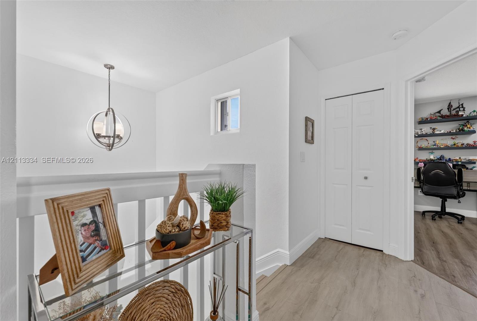 Hallway featuring wood-finish flooring, a contemporary spherical pendant light, a white bifold closet door, and a white baluster railing