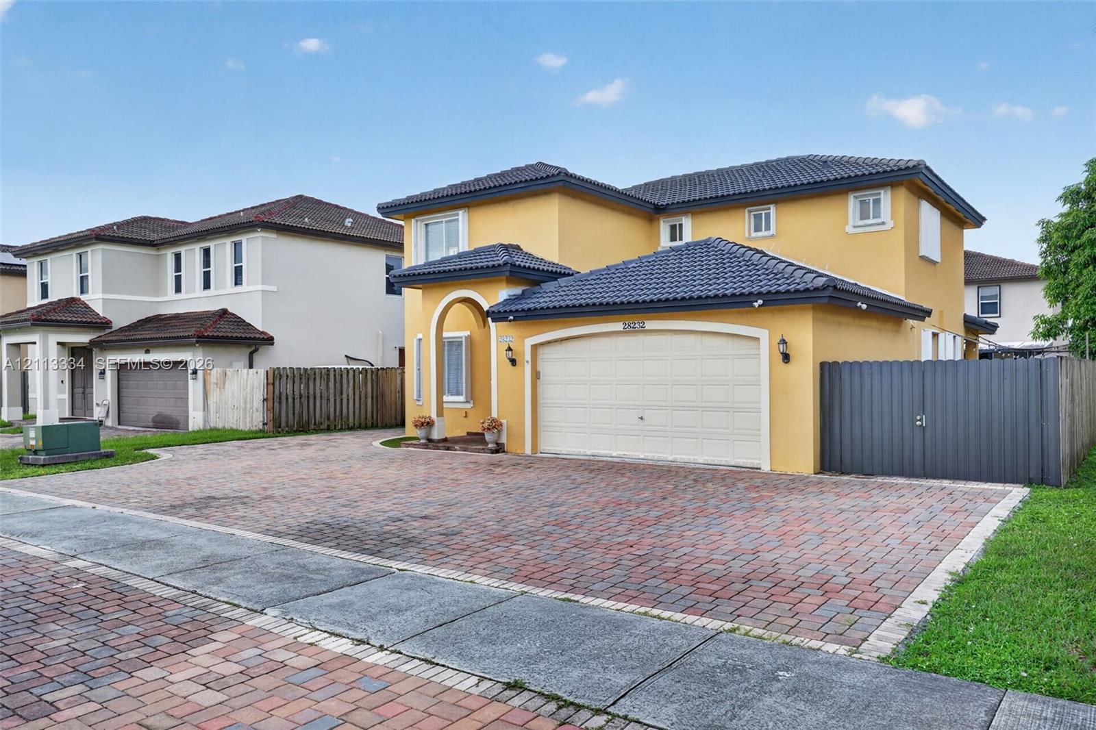 Two-story exterior featuring a stucco facade, tiled roof, arched entryway, and a multi-car brick paver driveway