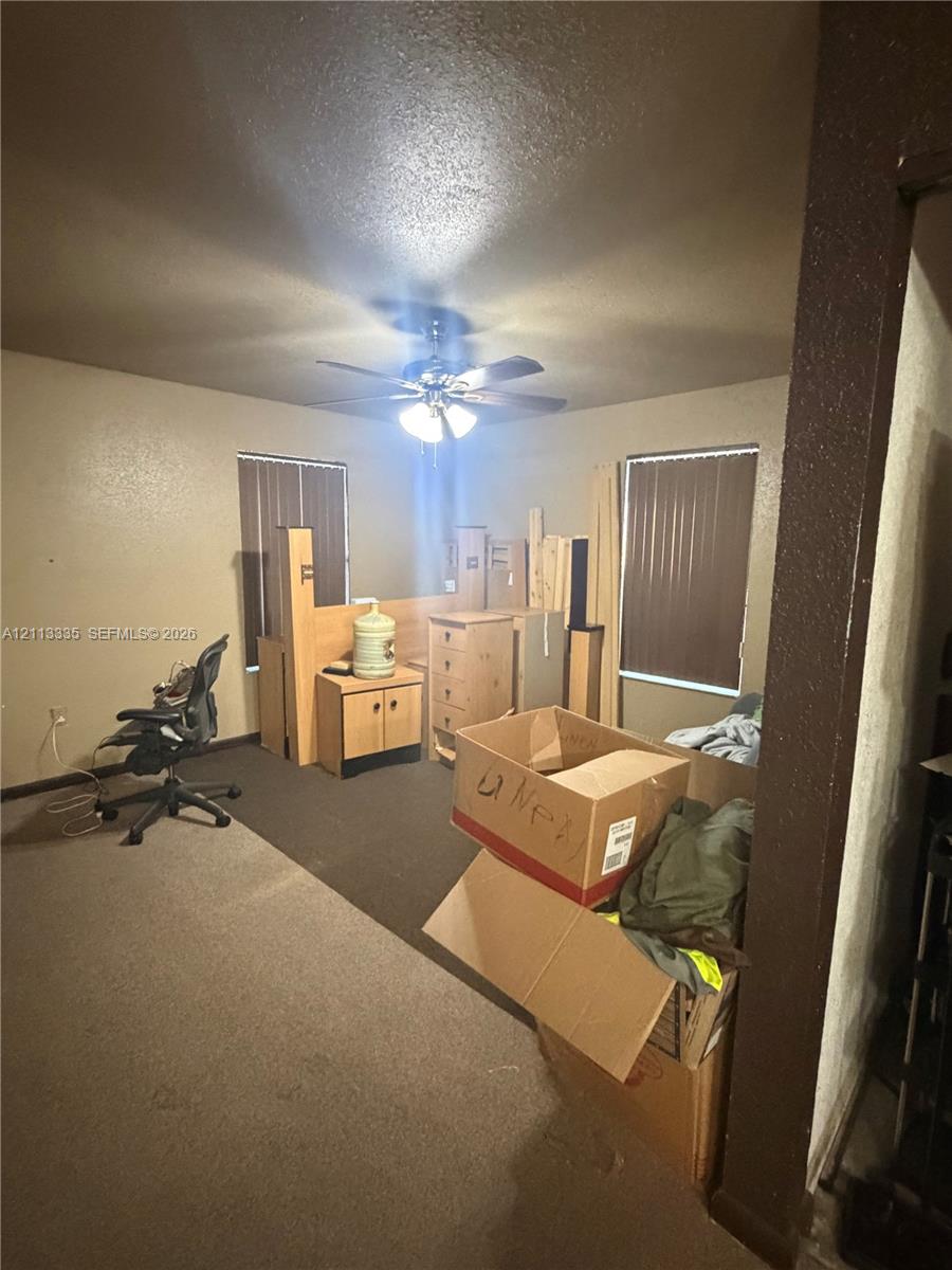 Room featuring neutral-toned carpeting, two windows with vertical blinds, and a ceiling-mounted fan with integrated light fixture