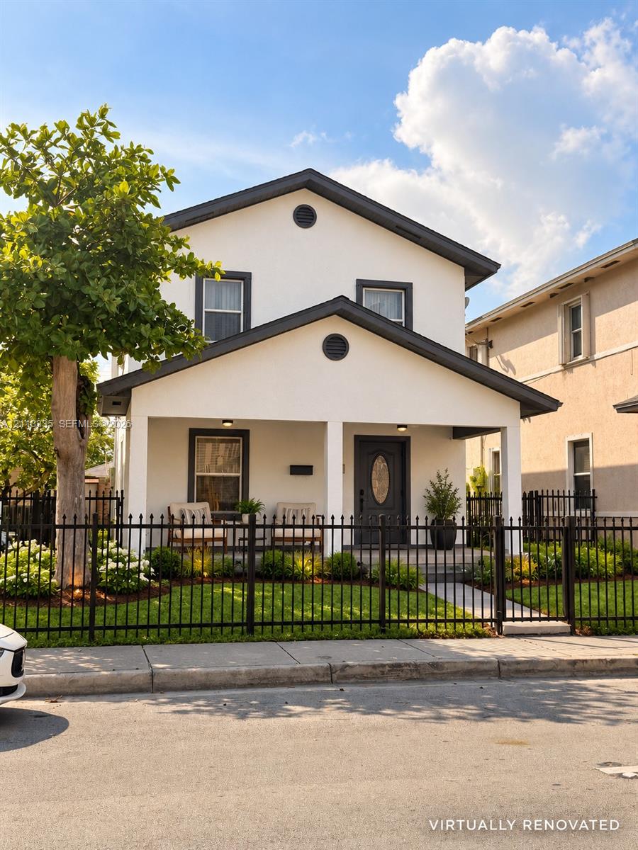 Two-story exterior featuring light-toned stucco facade, covered front porch with square columns, dark-trimmed windows, and decorative metal perimeter fencing Two-story exterior featuring light-toned stucco facade, covered front porch with square columns, dark-trimmed windows, and decorative metal perimeter fencing