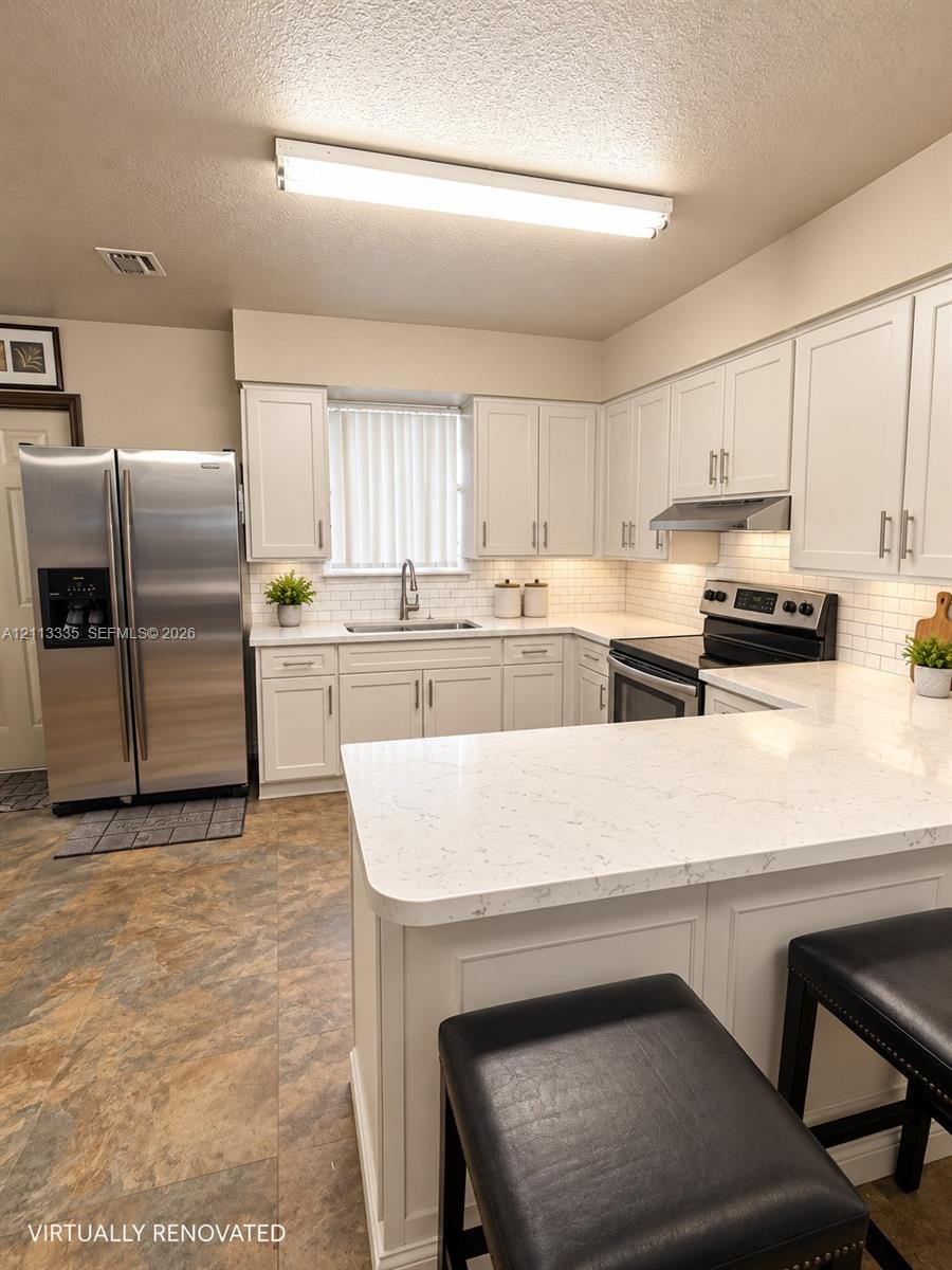 Kitchen featuring white shaker-style cabinetry, quartz countertops, subway tile backsplash, stainless steel refrigerator, and range with integrated hood Kitchen featuring white shaker-style cabinetry, quartz countertops, subway tile backsplash, stainless steel refrigerator, and range with integrated hood