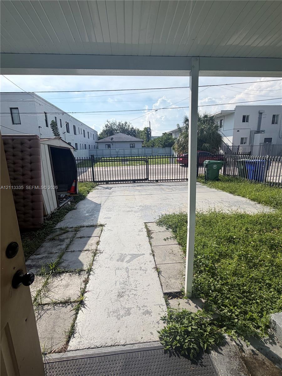 Covered porch entry featuring a concrete parking pad, metal security fencing, and gated access Covered porch entry featuring a concrete parking pad, metal security fencing, and gated access