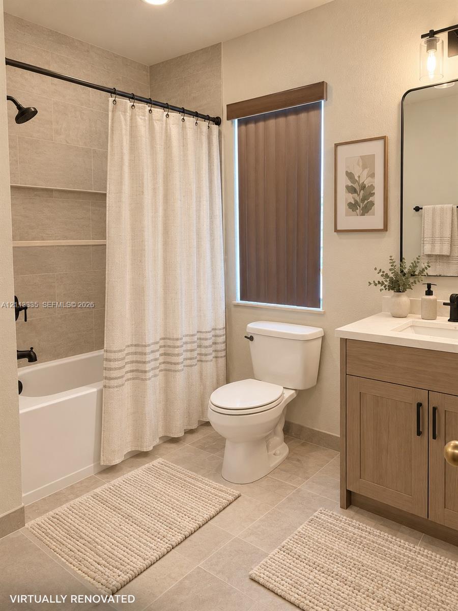 Bathroom featuring a vanity with a light wood-finish cabinet and solid surface countertop, matte black hardware, tile shower surround with integrated shelving, and large-format floor tile Bathroom featuring a vanity with a light wood-finish cabinet and solid surface countertop, matte black hardware, tile shower surround with integrated shelving, and large-format floor tile