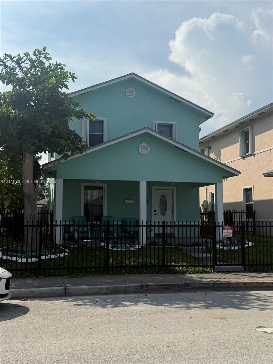 Two-story residence featuring a covered front porch, white support columns, dual-gabled roofline, and metal perimeter fencing Two-story residence featuring a covered front porch, white support columns, dual-gabled roofline, and metal perimeter fencing