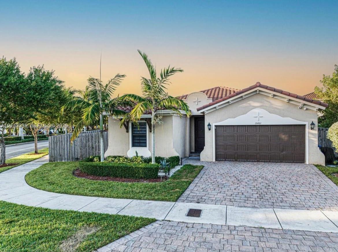 Stucco exterior featuring a clay tile roof, arched architectural detailing, paver driveway, and manicured landscaping Stucco exterior featuring a clay tile roof, arched architectural detailing, paver driveway, and manicured landscaping