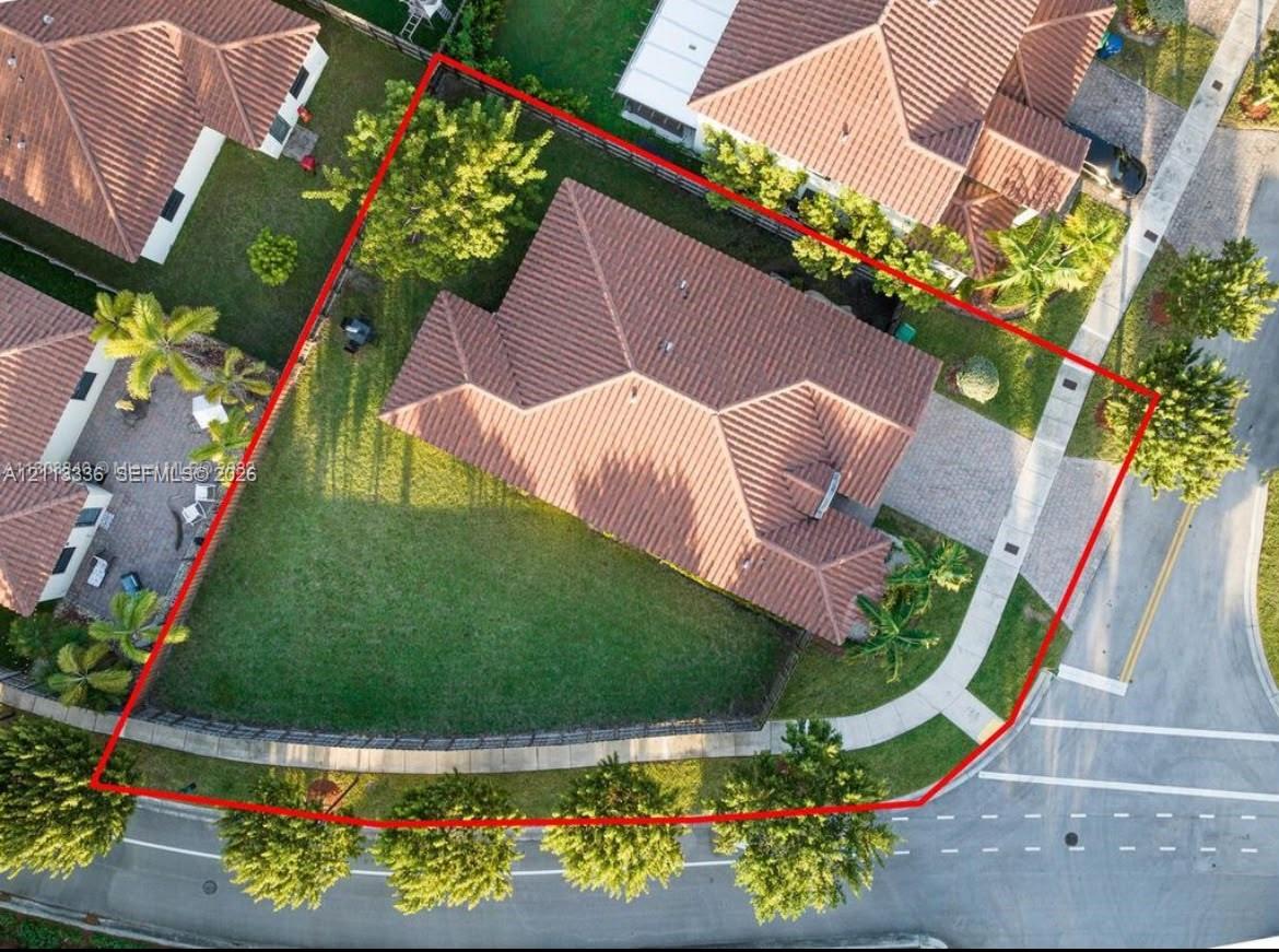 Corner lot property featuring a multi-hipped tile roof, paved driveway, expansive lawn, and perimeter fencing