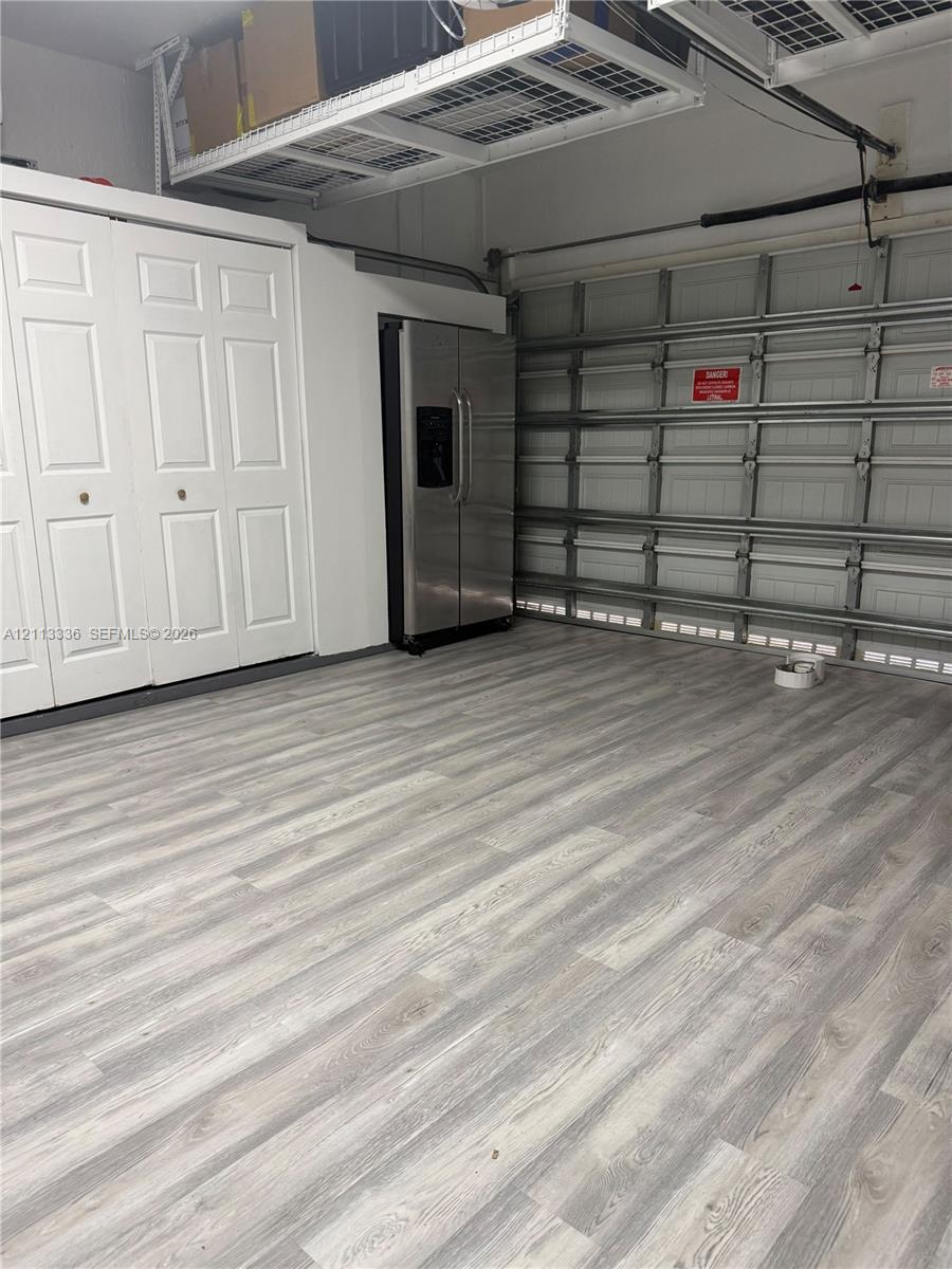 Garage area featuring wood-finish flooring, built-in white dual-panel closet doors, stainless steel refrigerator, and overhead wire storage shelving