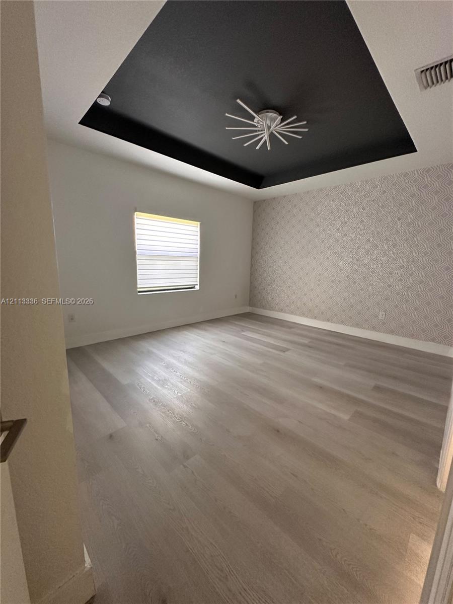 Tray ceiling with matte black finish, modern starburst flush-mount lighting, wood-finish flooring, and patterned accent wallpaper