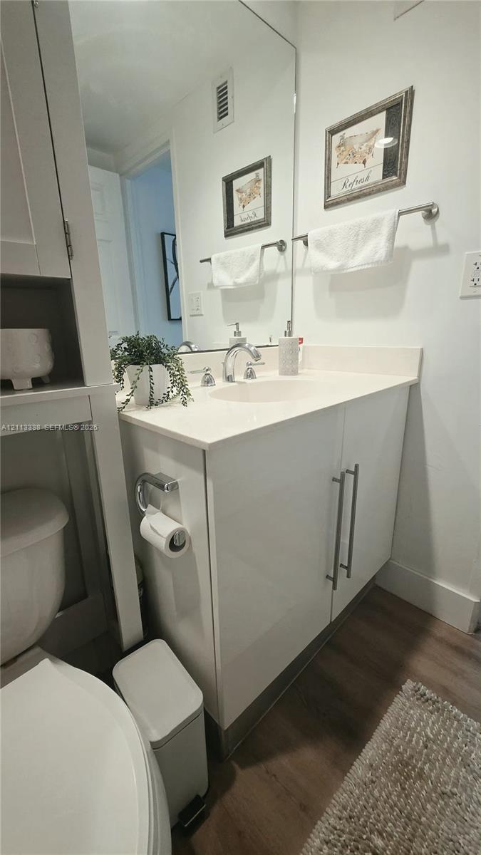 Vanity featuring a white cabinetry base, integrated sink, countertop, and polished hardware, complemented by a floor-to-ceiling mirror and wood-finish flooring