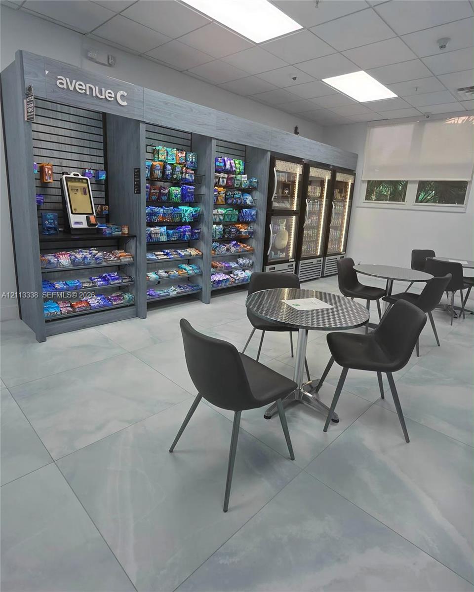 Built-in shelving unit with integrated electronic payment kiosk, commercial-grade reach-in glass door refrigeration, drop ceiling with recessed lighting, and large-format tile flooring