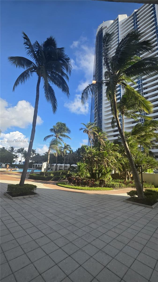 High-rise building exterior featuring tiered balconies, paved terrace, mature palm trees, and manicured landscaping
