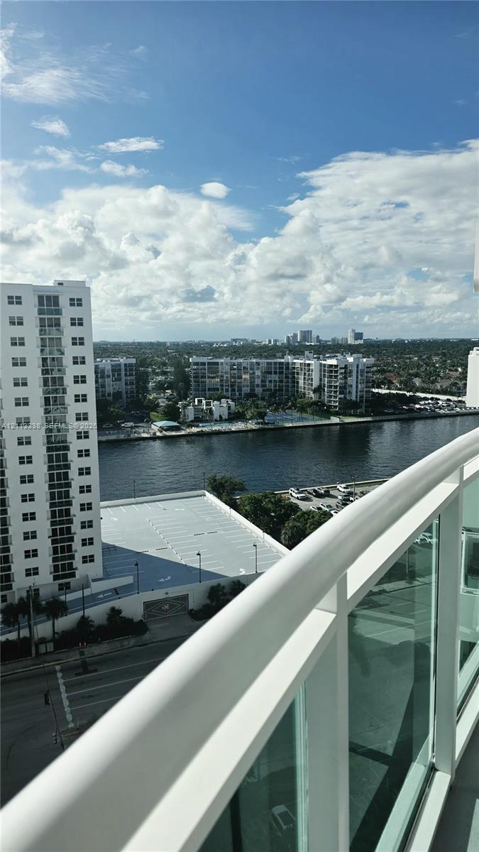 Elevated balcony with glass panel railing and painted metal frame overlooking waterway and urban skyline