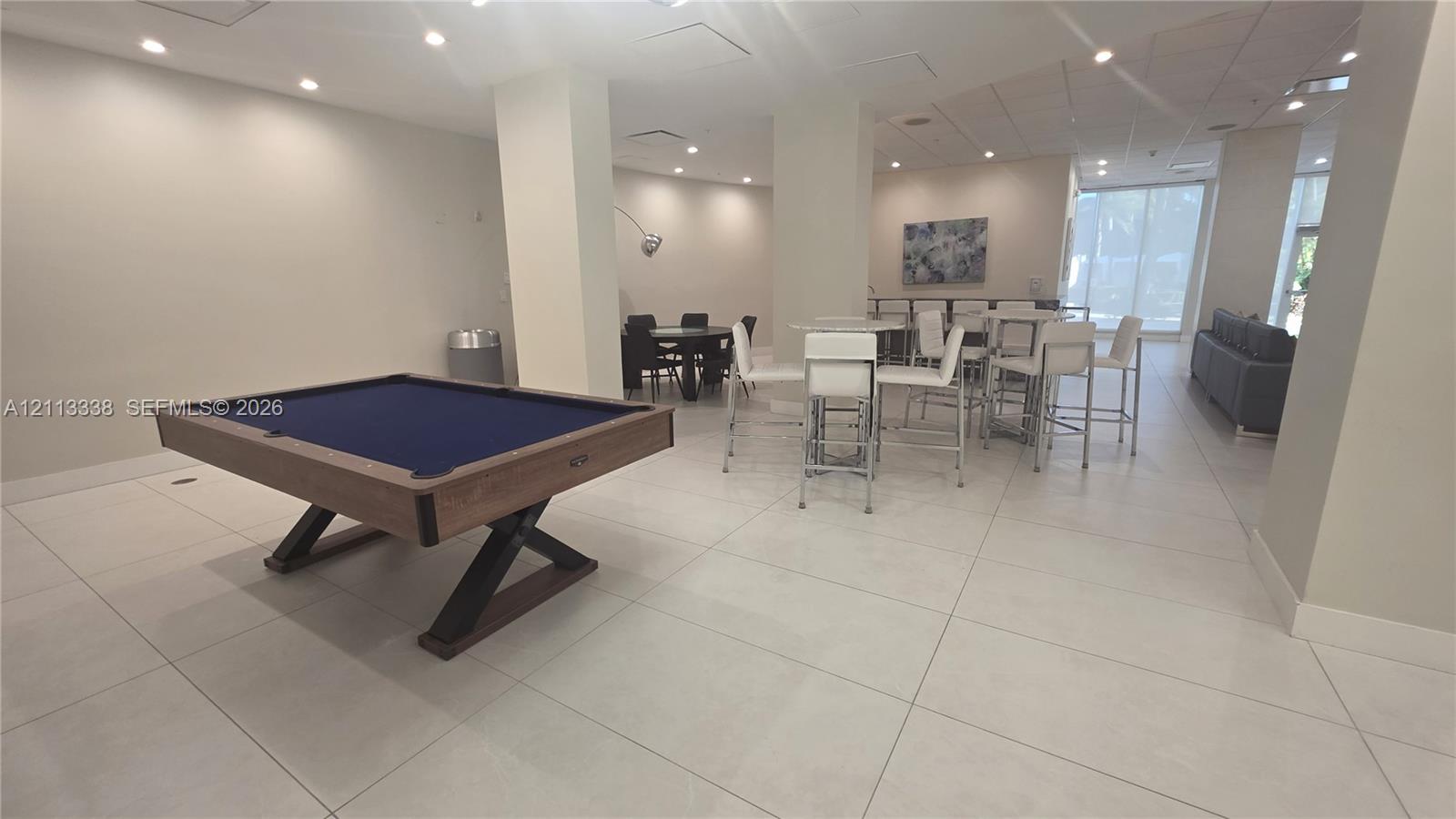 Large common area featuring tile flooring, recessed ceiling lighting, structural support columns, and expansive windows