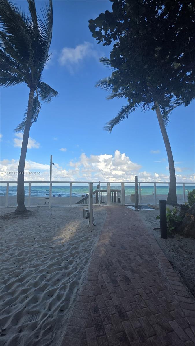 Brick paver pathway leading to a gated entry point with direct beach access, accented by mature palm trees