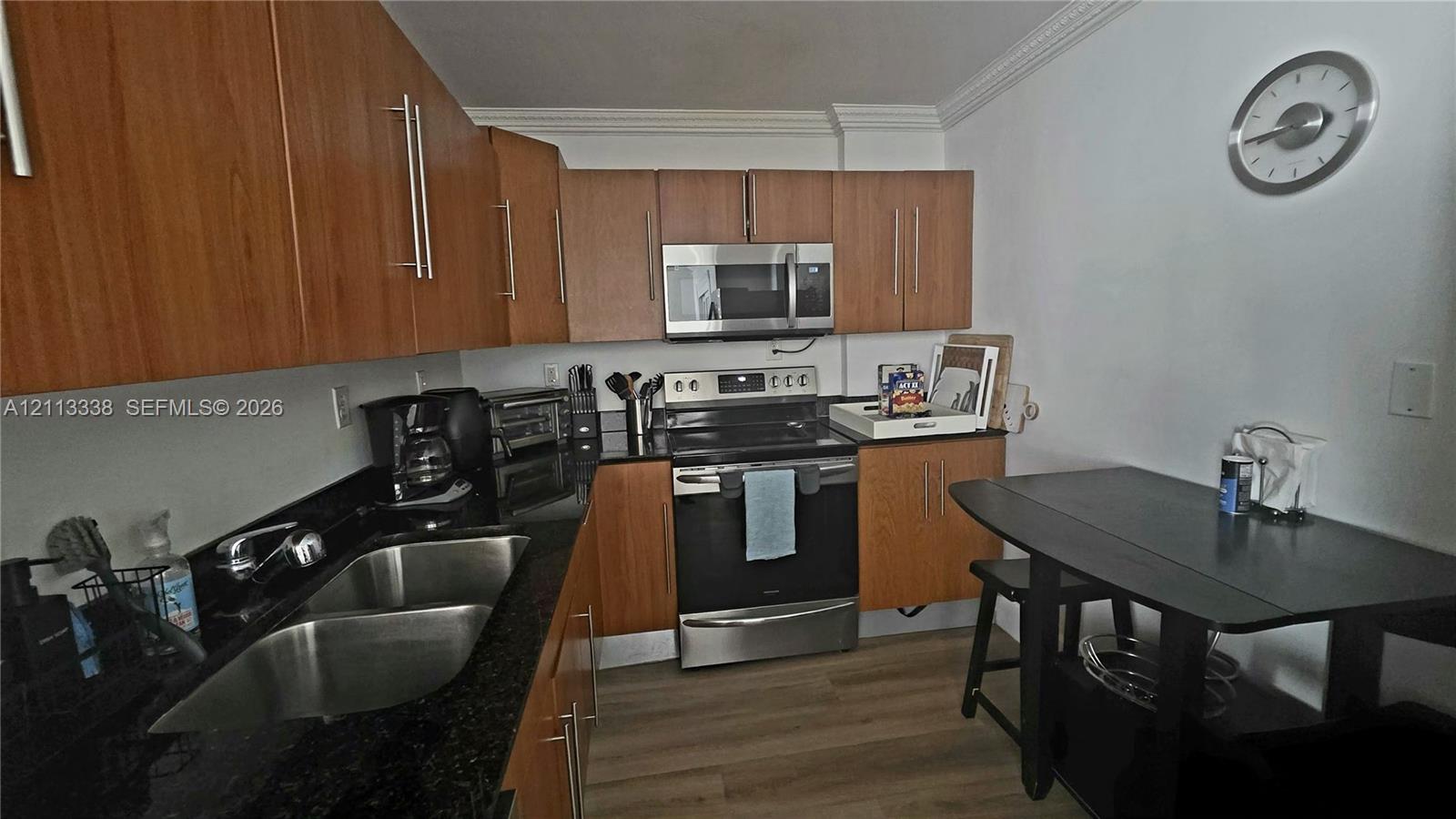 Kitchen featuring wood-finish cabinetry, dark stone countertops, stainless steel appliances, dual-basin sink, and light-toned wood-finish flooring