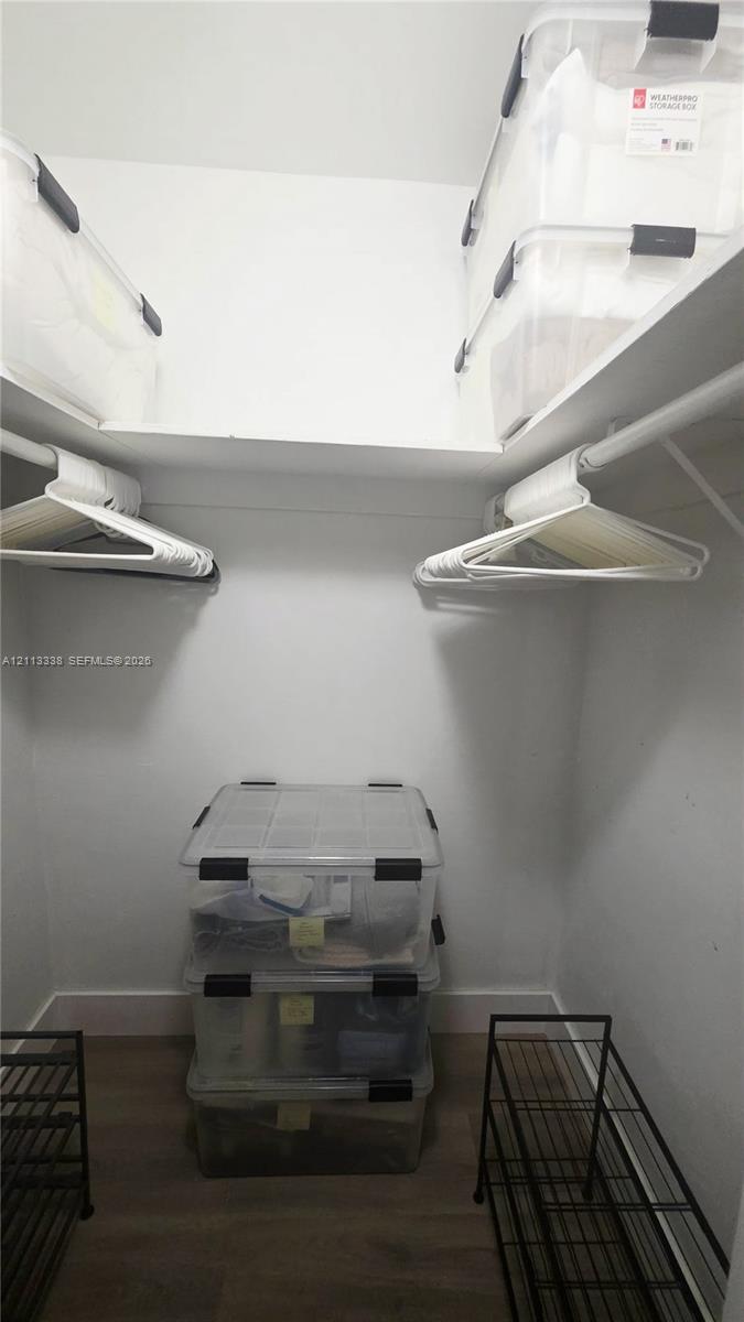 Storage area featuring wood-finish flooring, two levels of built-in shelving, and white hanging rods
