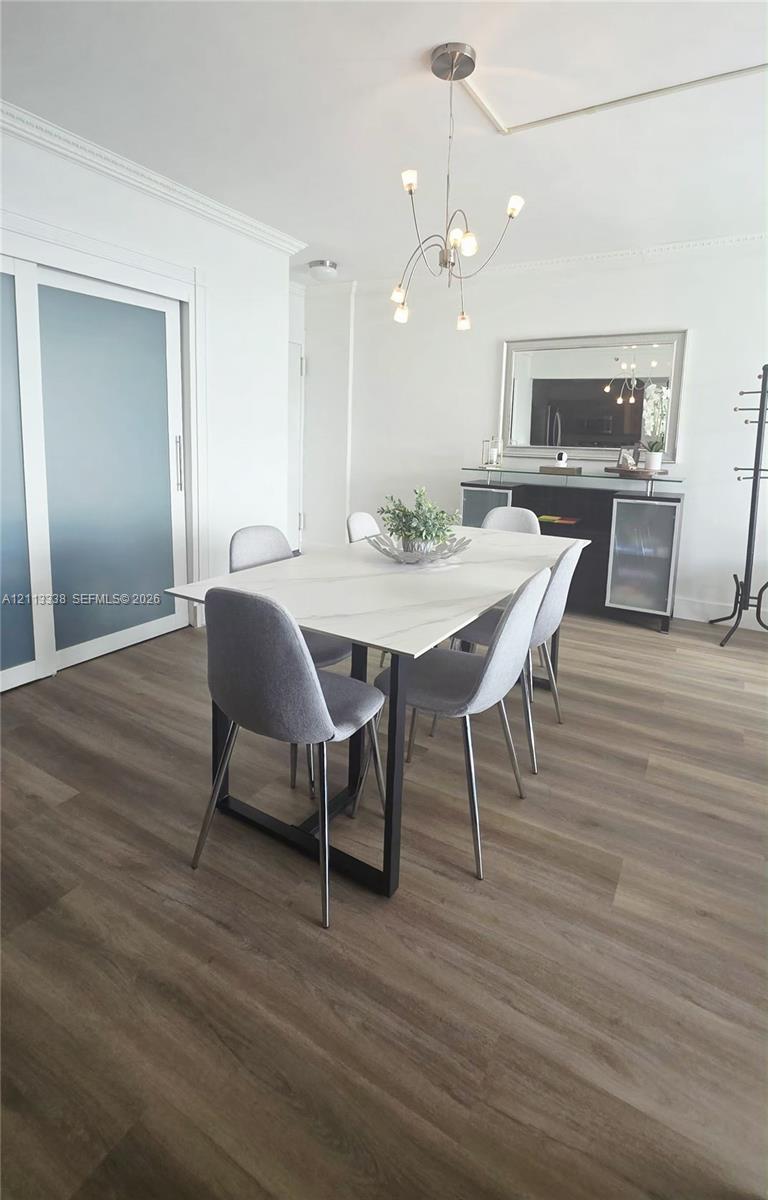 Wood-finish flooring, sliding opaque glass door, crown molding, and modern multi-arm chandelier