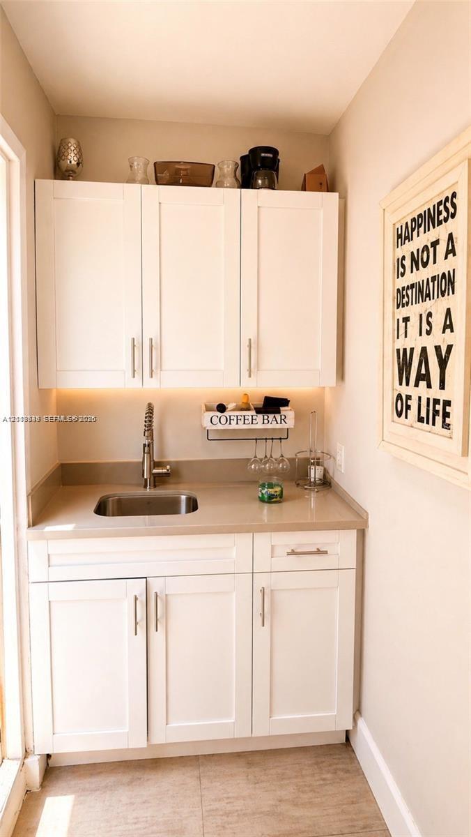 Built-in white cabinetry featuring shaker-style doors, matte-finish countertop, integrated stainless steel sink, gooseneck faucet, and under-cabinet lighting