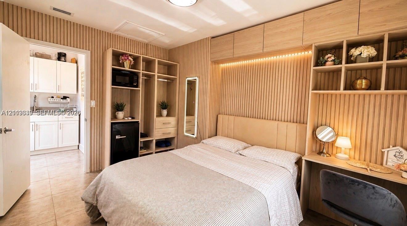 Built-in floor-to-ceiling slatted wood-finish cabinetry, integrated desk, neutral tile flooring, and custom overhead recessed lighting