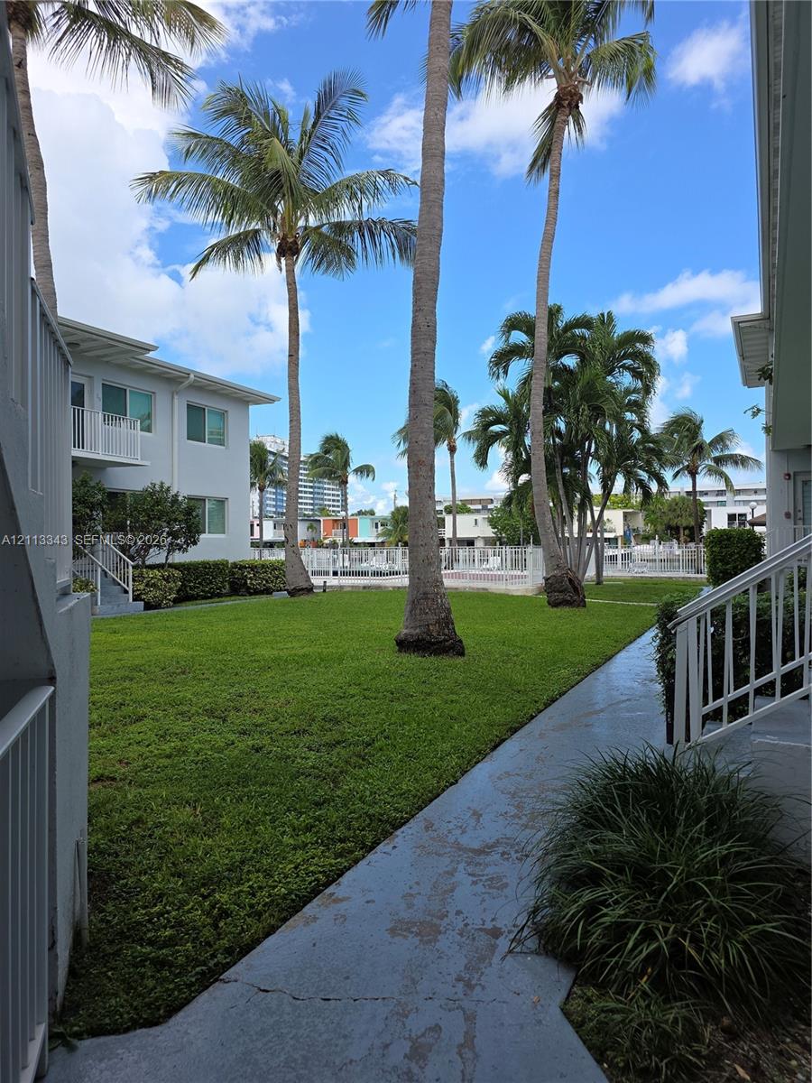 Expansive common area featuring a manicured lawn, mature palm trees, exterior stairs, and a metal-fenced swimming pool