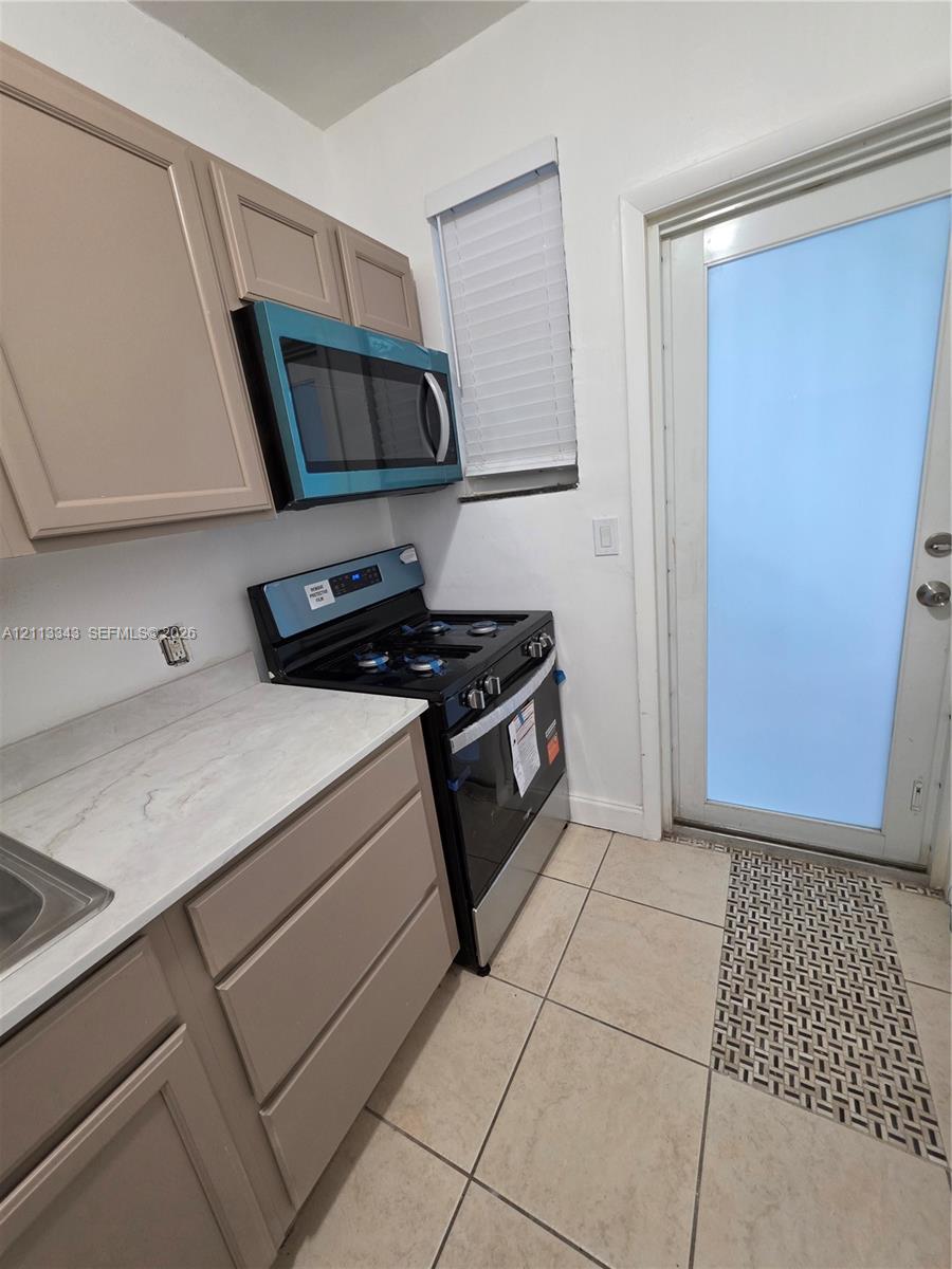 Kitchen area featuring light-toned cabinetry, solid surface countertops, a full-size range, an integrated over-the-range microwave, and ceramic tile flooring