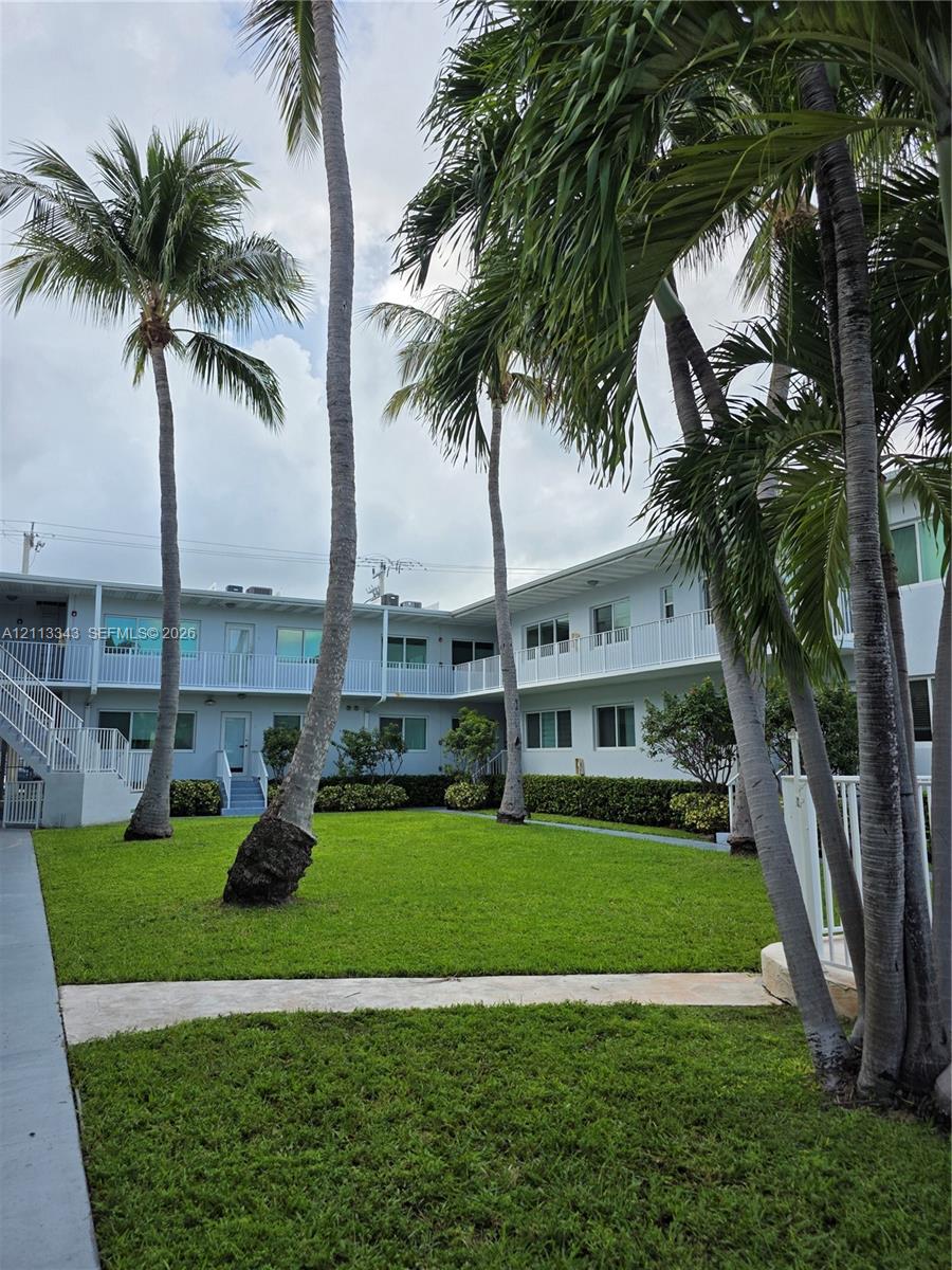 Courtyard featuring a manicured lawn, established palm trees, concrete walkways, and perimeter shrubbery