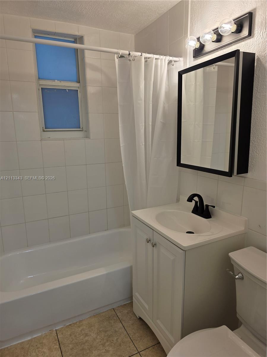 Bathroom featuring white wall-tile surround, vanity with integrated basin, matte black hardware, medicine cabinet, and three-bulb vanity light fixture