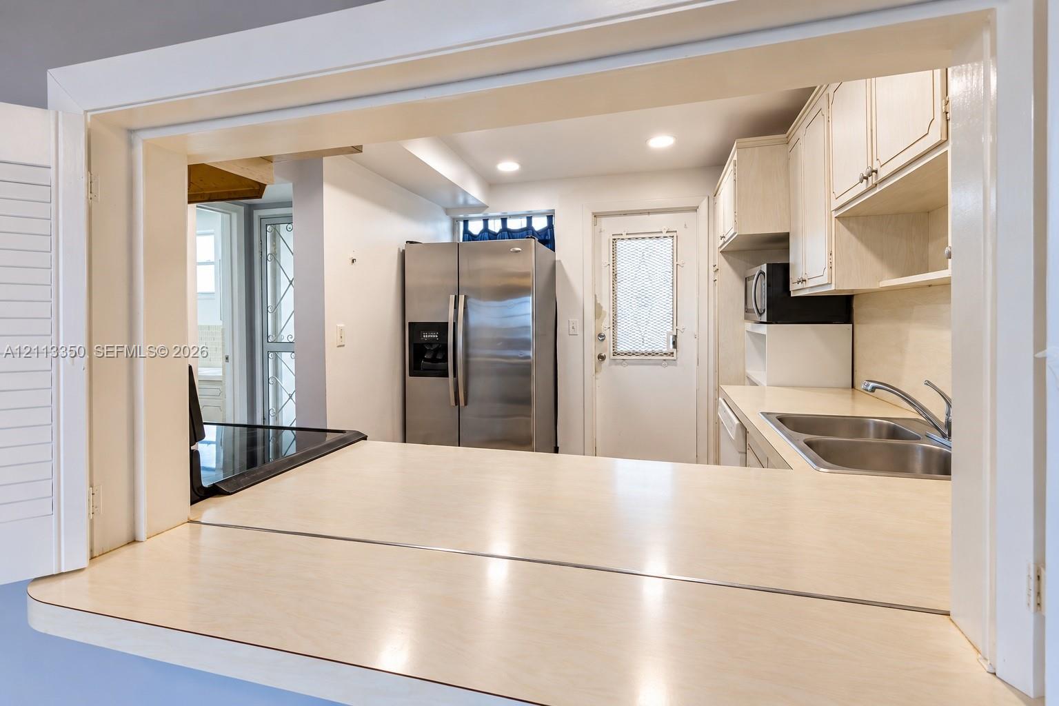Kitchen featuring a pass-through counter, stainless steel refrigerator, double basin sink, and white cabinetry